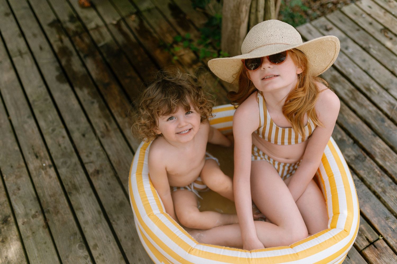 People relaxing on wooden deck with sun hats and yellow striped towels.