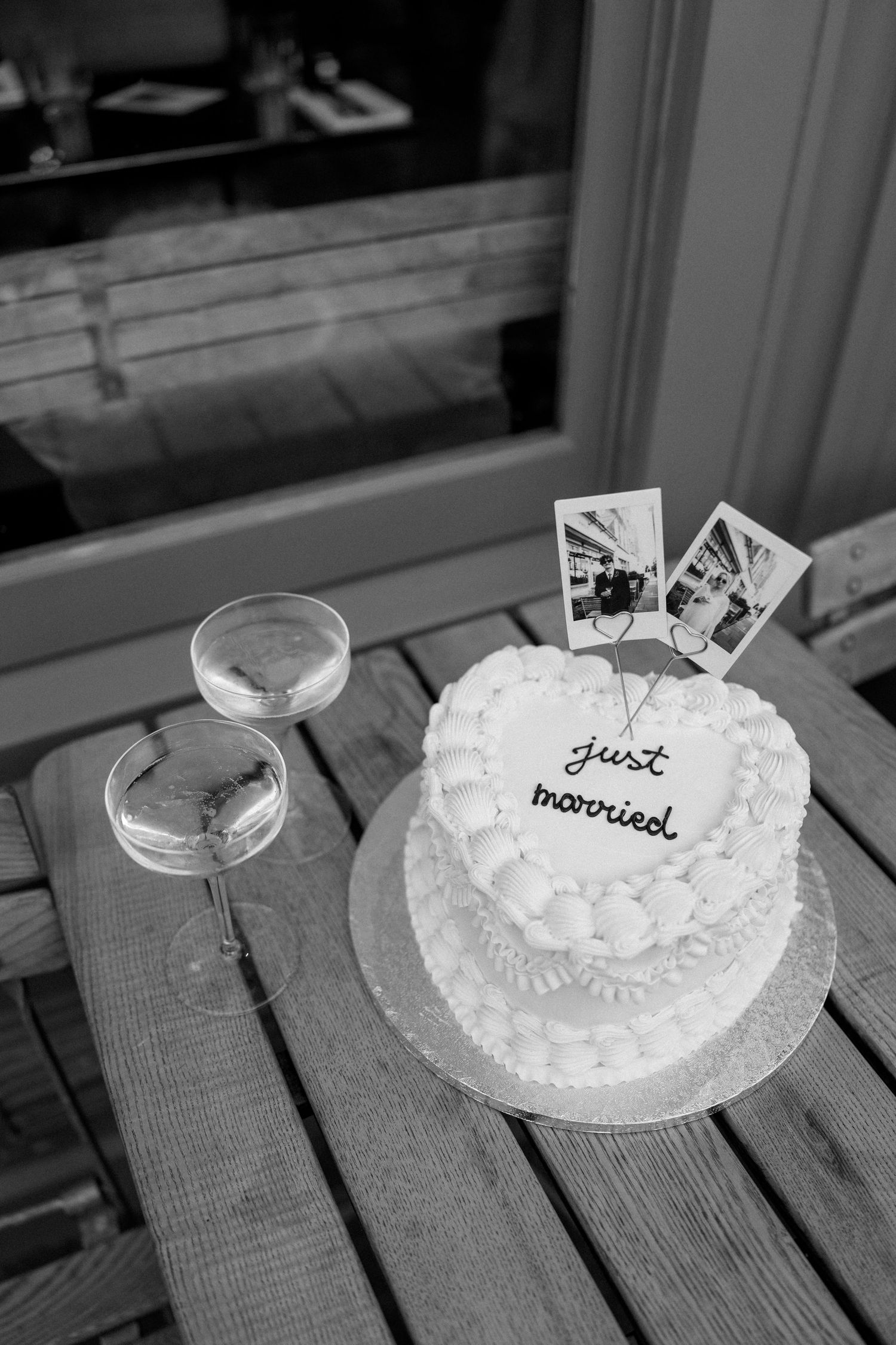 A white wedding cake with 'Just Married' text and two champagne glasses on a wooden table.