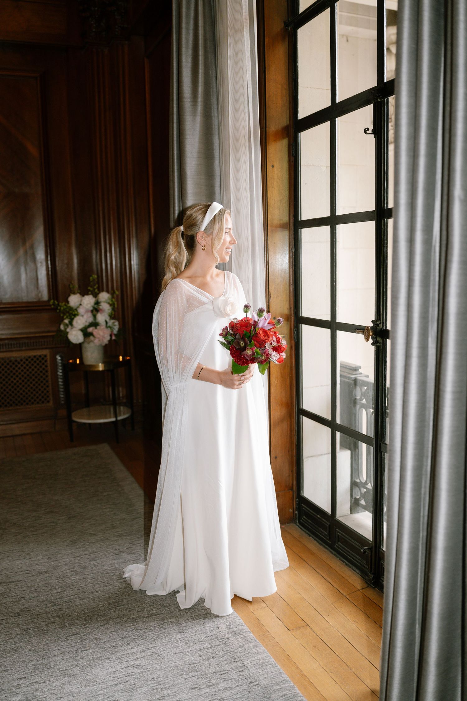 Wedding photography sequence near large windows showing flowing white dress and red floral bouquet.