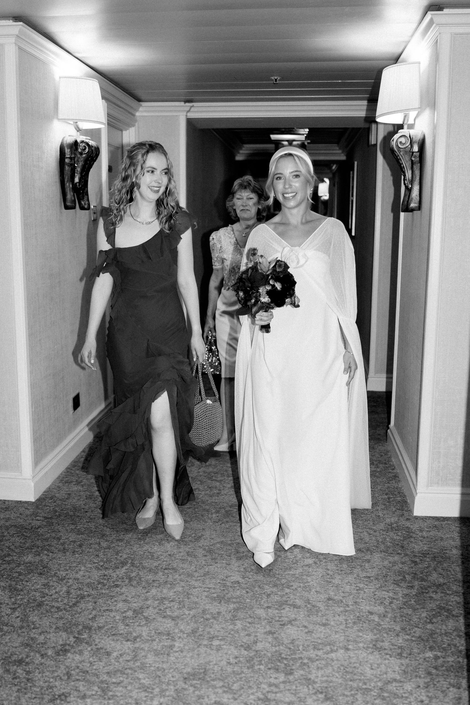 Wedding party walking through elegant hotel hallway in formal attire.