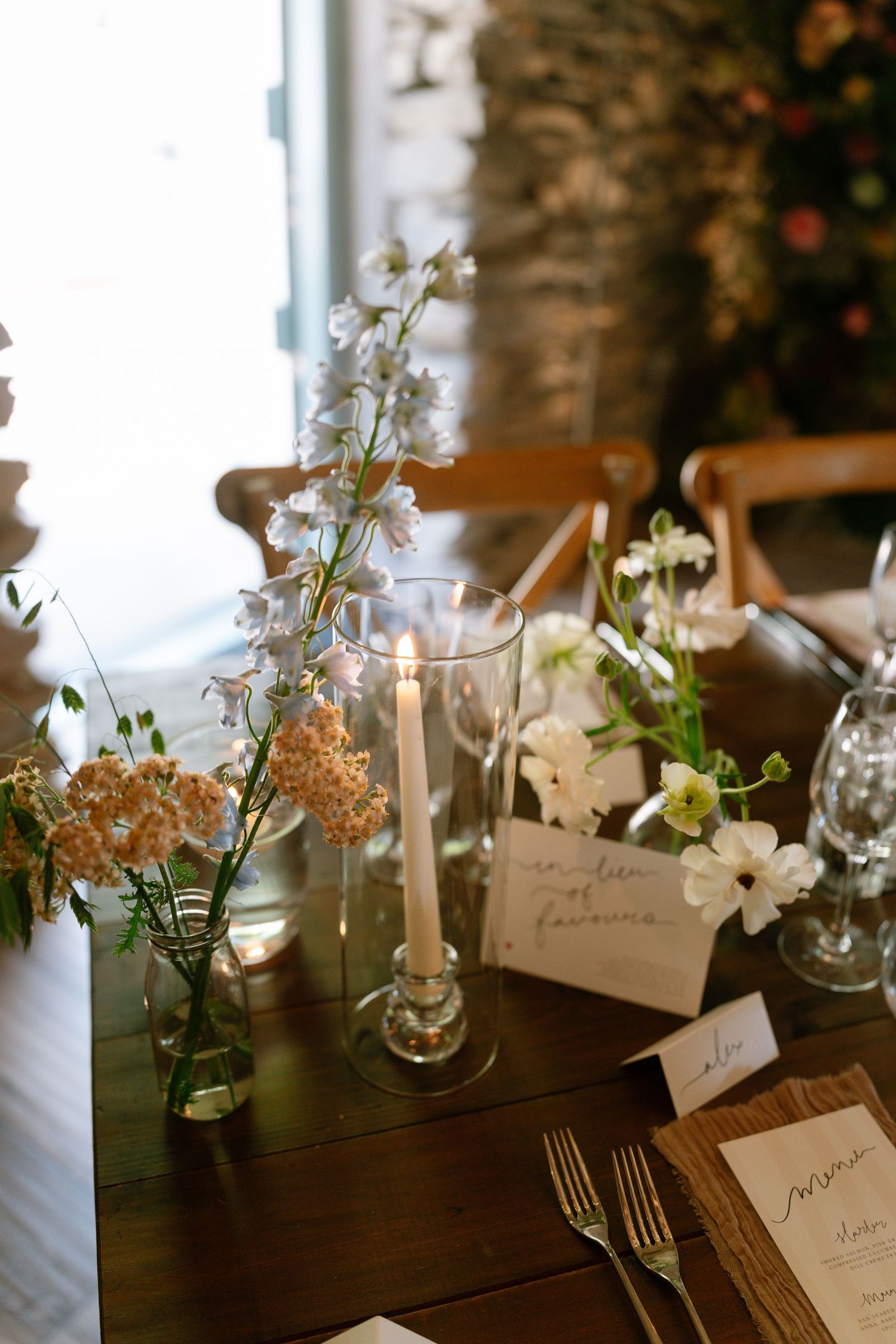Elegant wedding table setting with white floral centerpieces and handwritten place cards on a dark wooden surface.