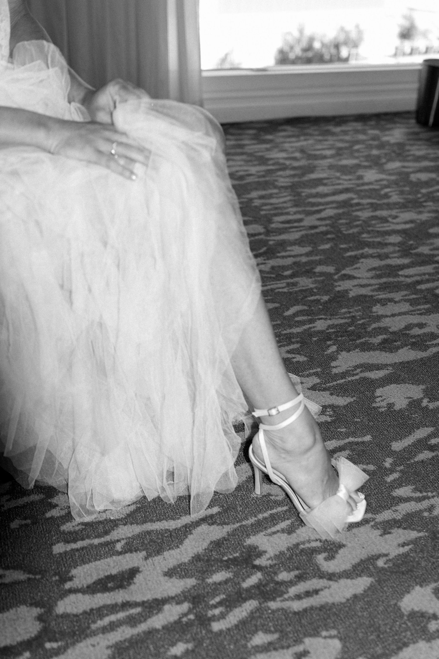 Close-up of bridal shoes and tulle dress hem on patterned carpet.