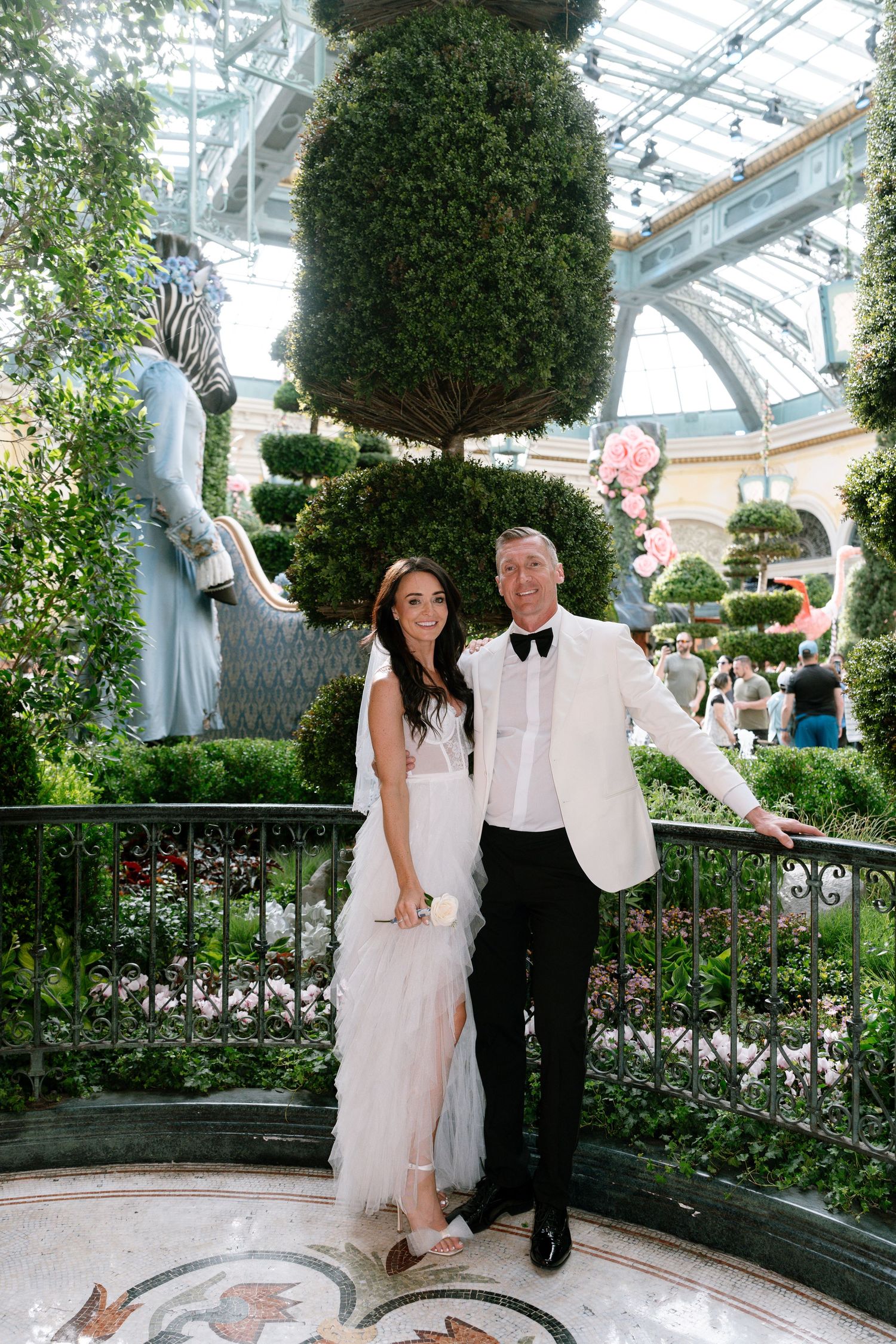 Wedding couple posing in a lush greenhouse garden with topiary trees.