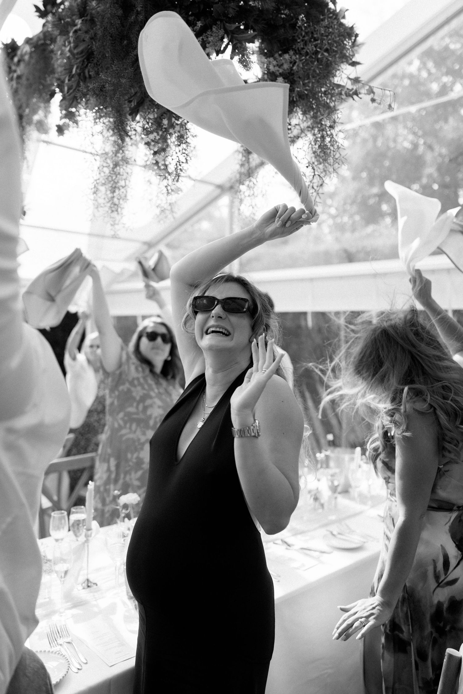 Wedding guests celebrating and waving napkins during a festive reception under a decorated tent.