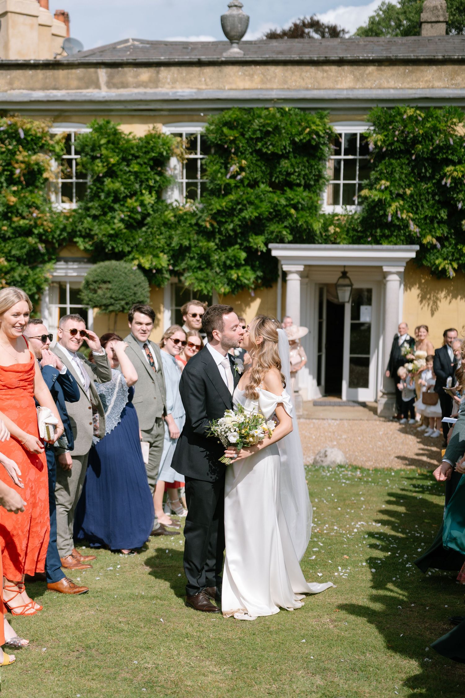 Wedding party and guests gather on a lawn outside an elegant country house for the celebration.