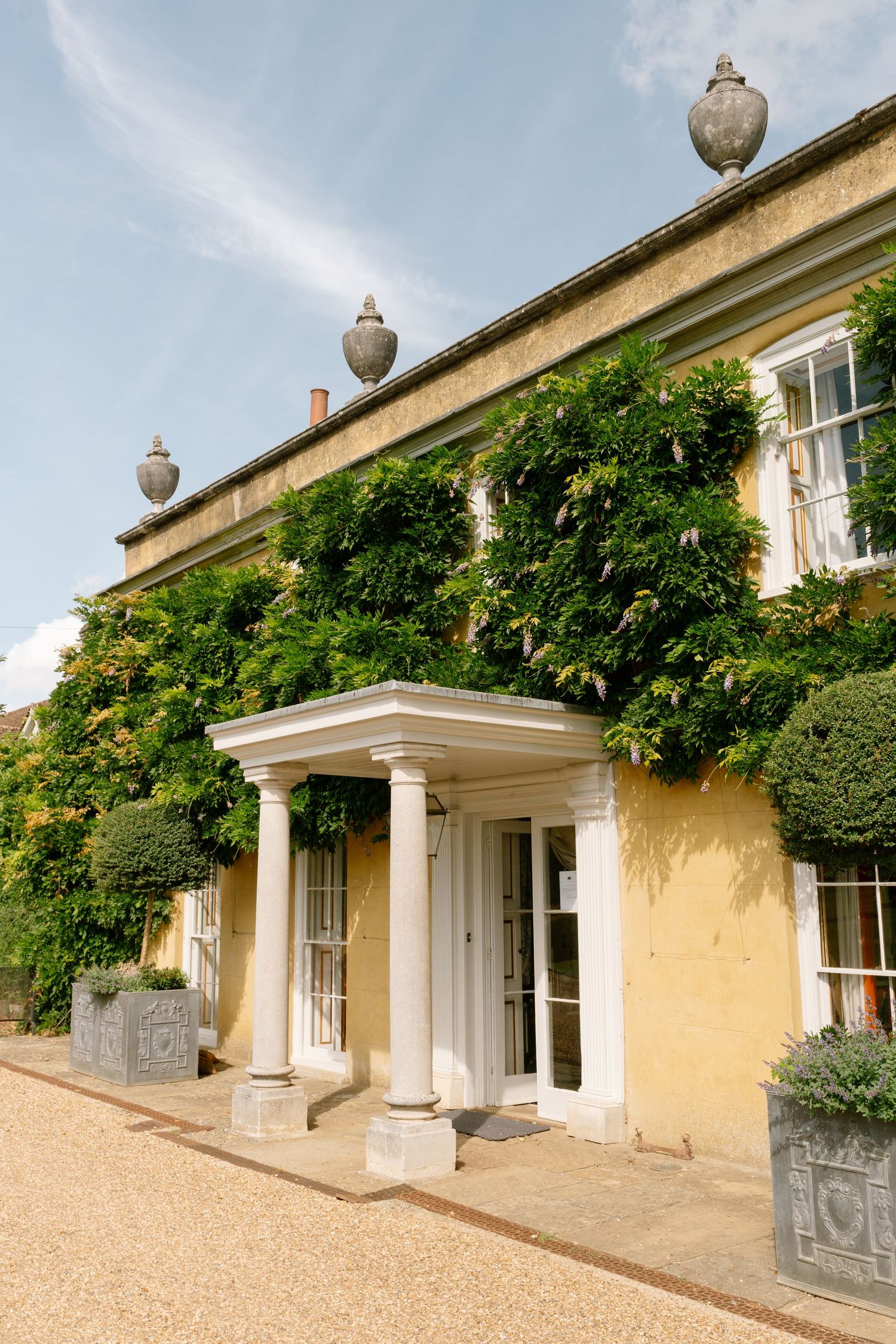 Classical columned entrance with ivy-covered walls of a yellow Georgian manor house.