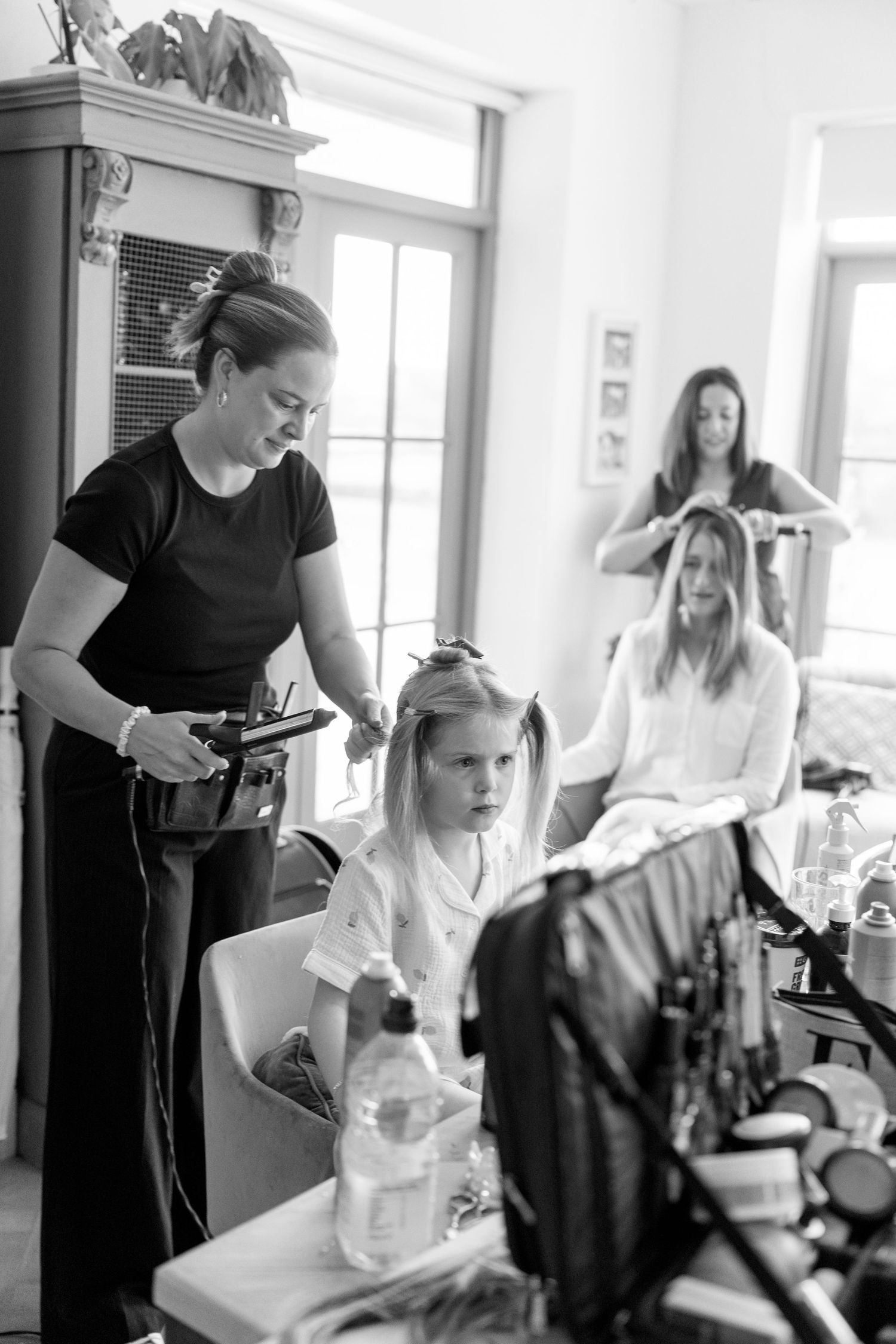 Behind the scenes of bridal hair and makeup preparation with stylists working in a bright room.