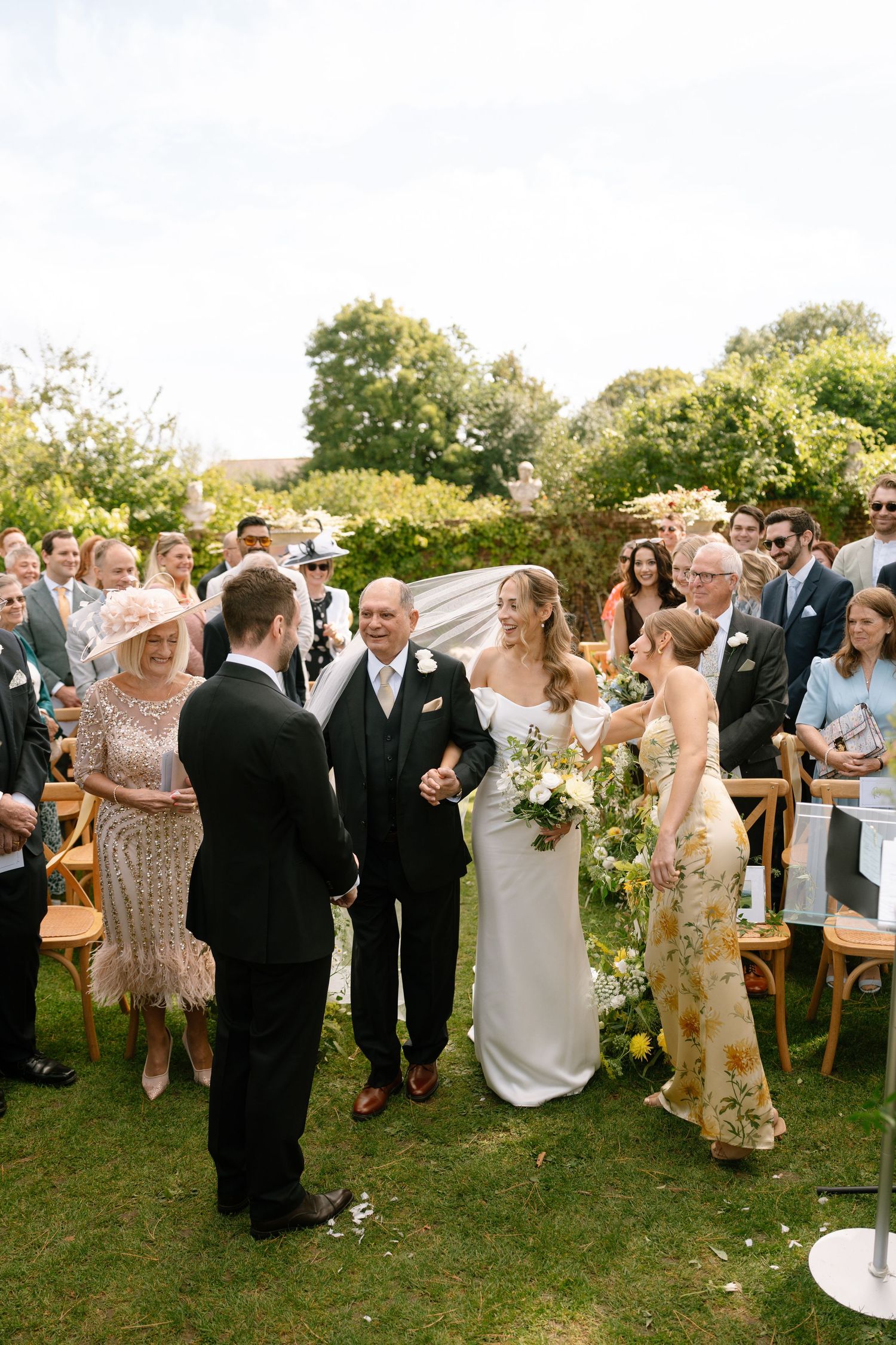 Guests celebrating at an outdoor wedding reception with floral decorations and wooden chairs.