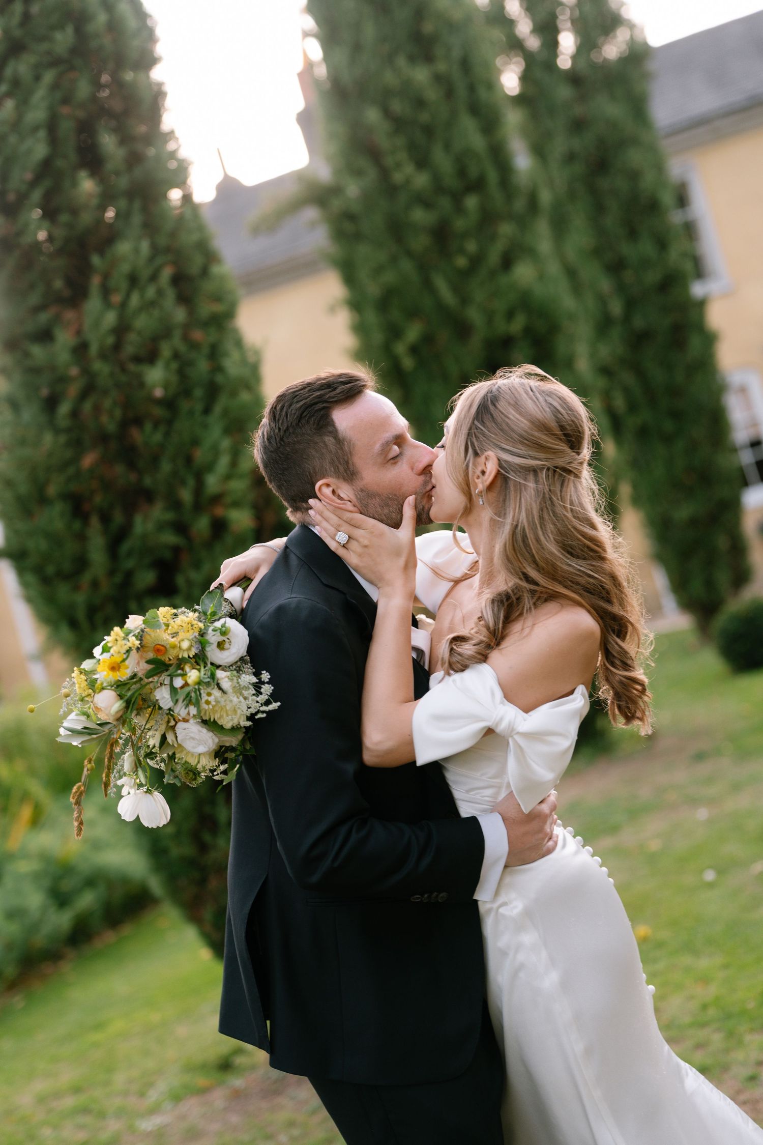 A tender wedding moment captured in a garden with cypress trees at sunset.