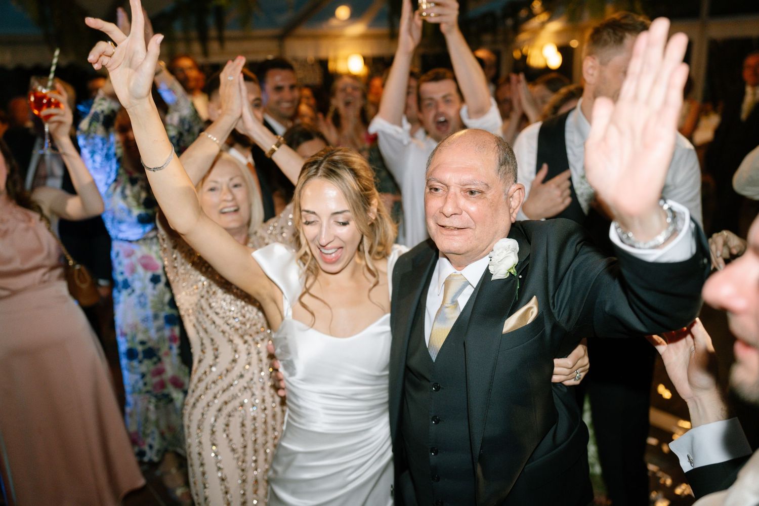 Energetic wedding celebration with guests dancing and cheering under decorative foliage.