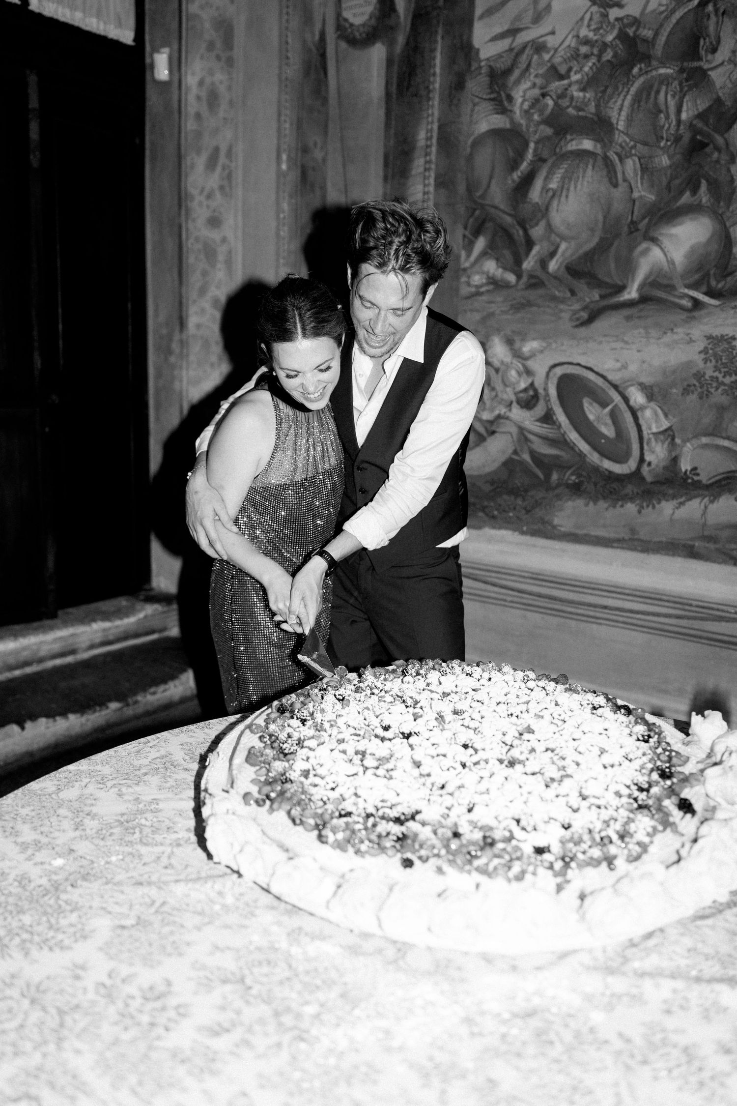 A couple leans over a large decorated cake at a formal celebration.