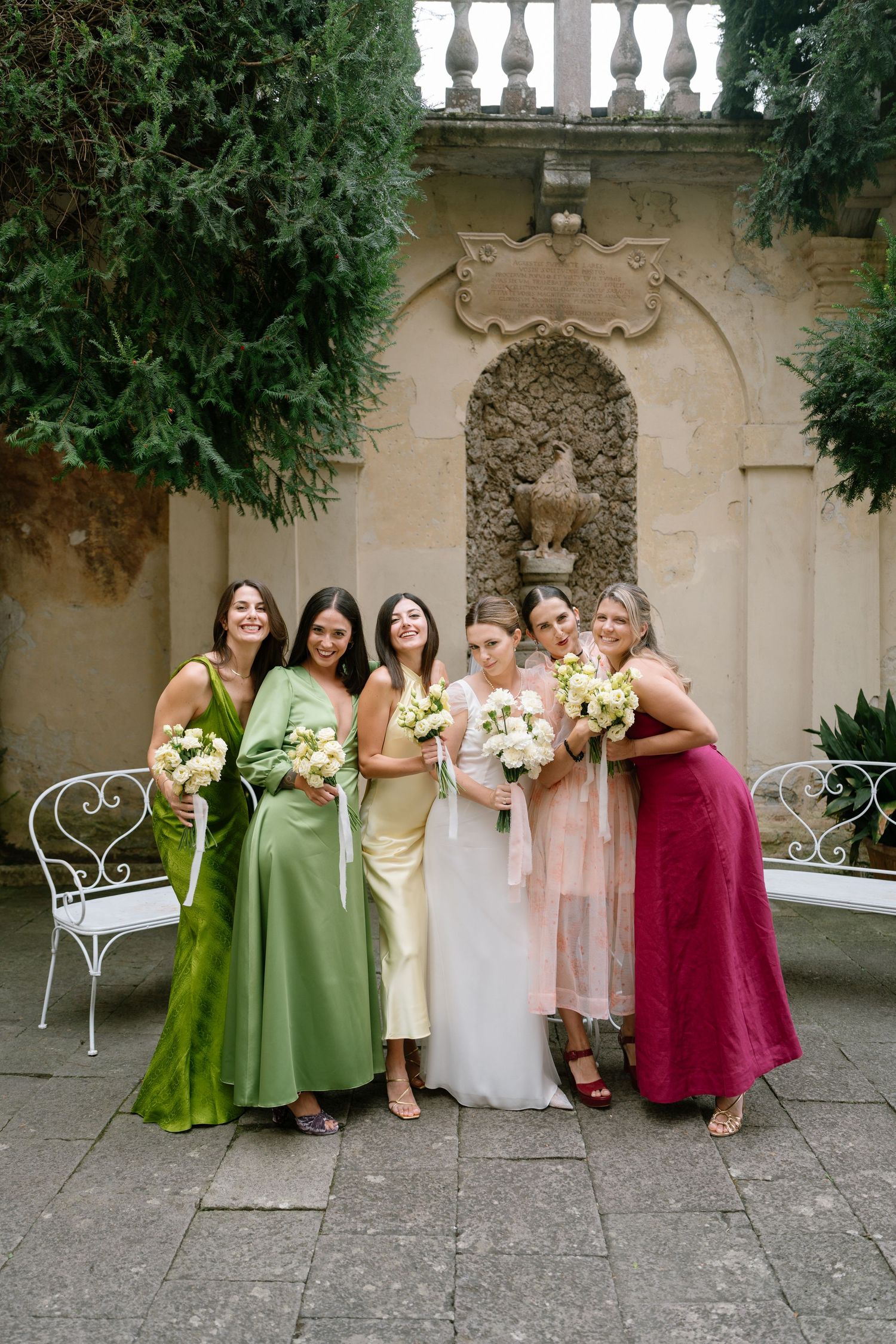 Bridesmaids in colorful dresses pose together in a Mediterranean-style courtyard.