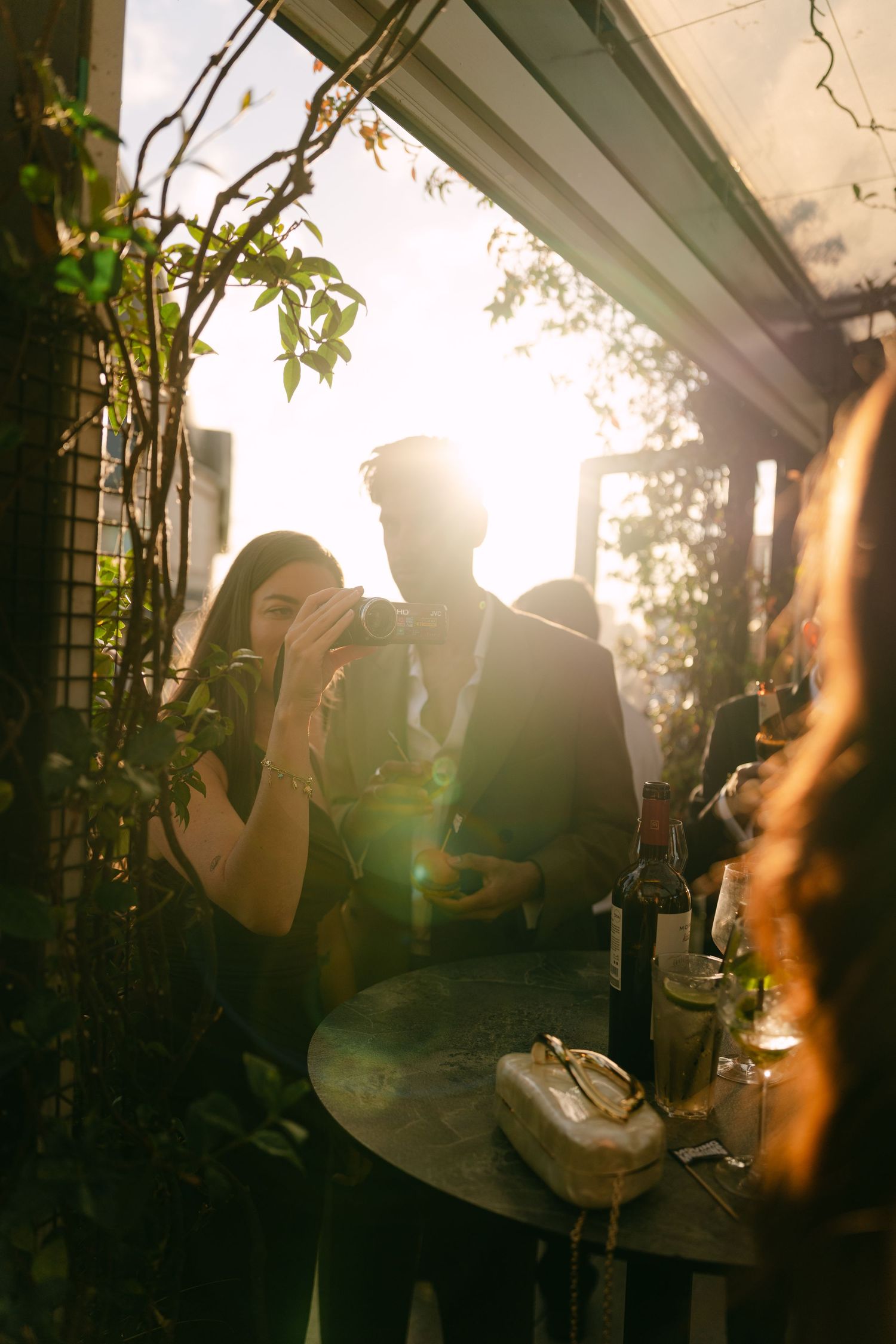 Guests enjoying a sunset wedding reception with vine-covered pergola and golden light.