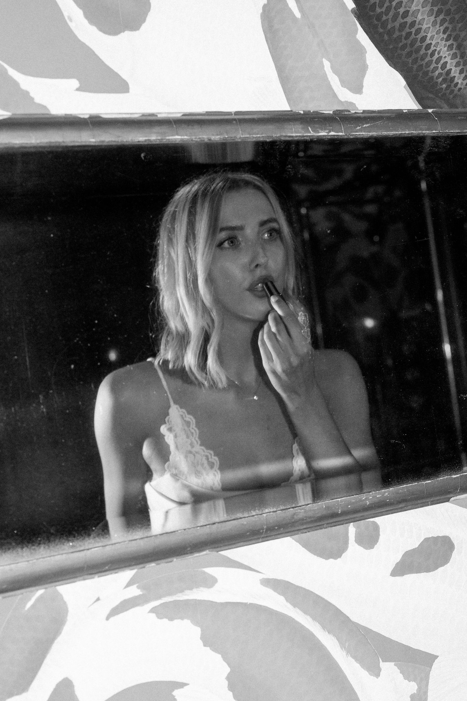 Black and white photo of blonde bride applying lipstick while reflected in vintage mirror.