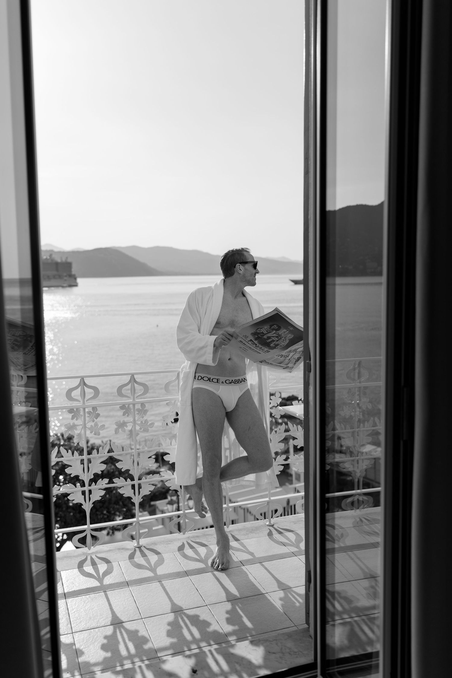 Black and white photo of a man in Dolce Gabbana underwear on a balcony with sea views.