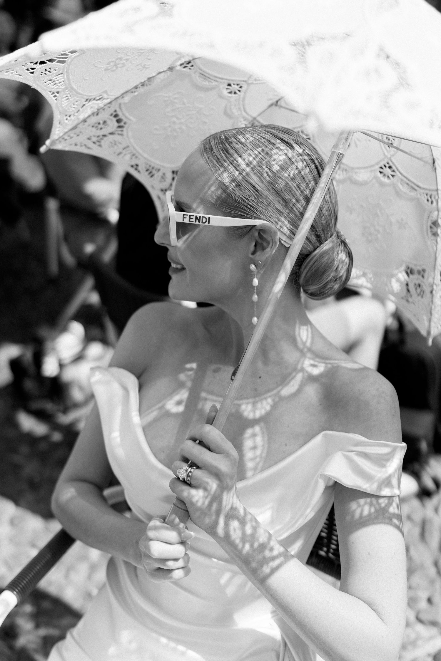 Black and white portrait of a blonde bride holding a lace parasol wearing Fendi sunglasses at outdoor wedding.
