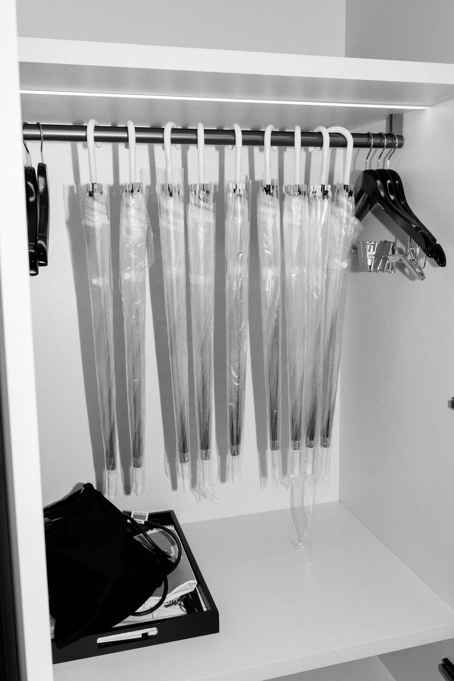 Clear plastic garment bags hang neatly on a white closet rod against a white wall, creating an organized storage solution.
