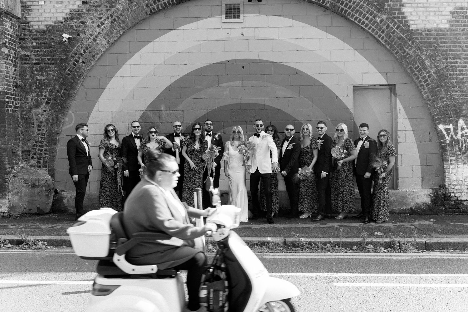 Wedding party gathers under brick archways for formal group photos.