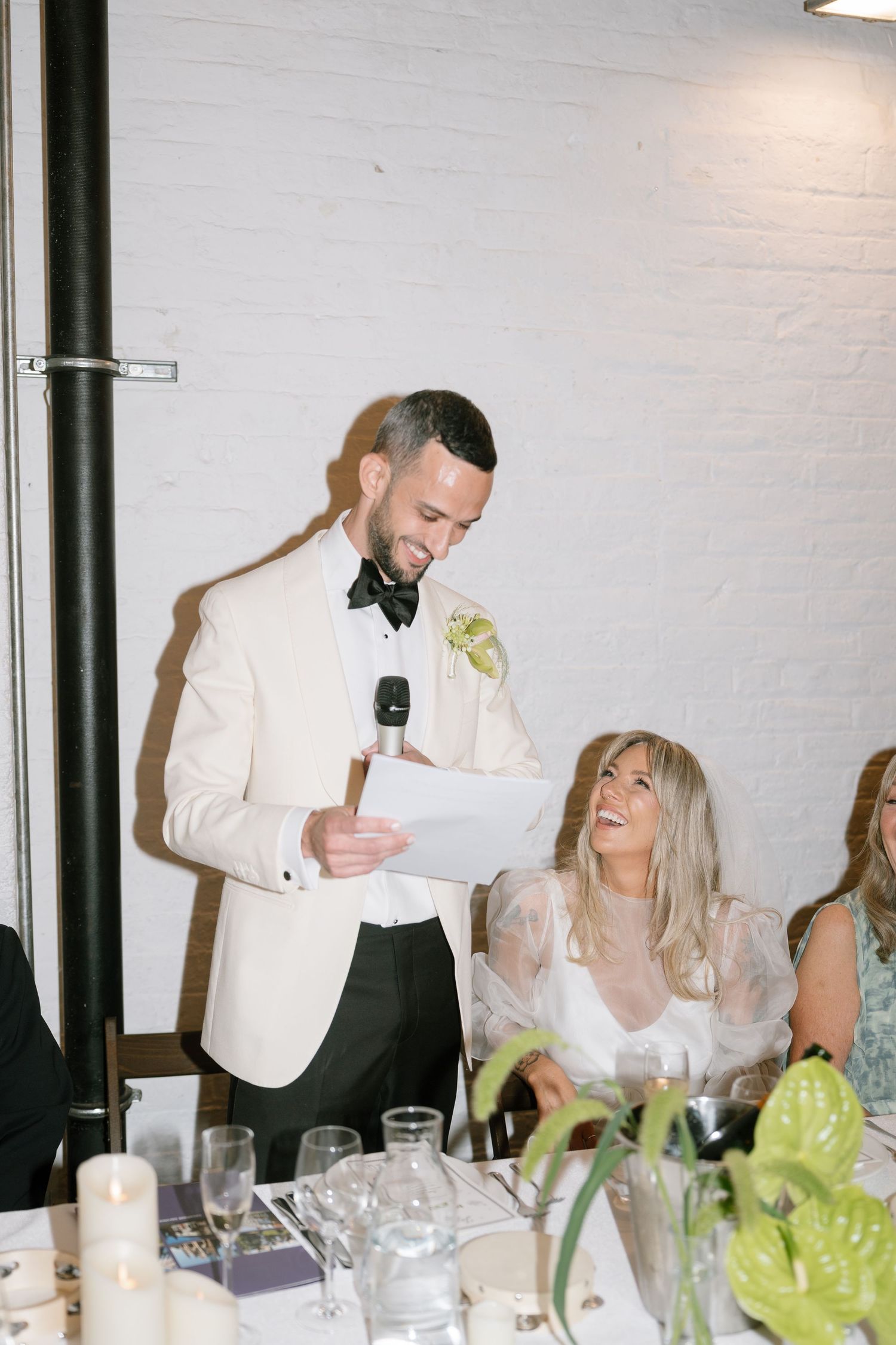 Wedding guests seated at a reception table with white tablecloths and floral centerpieces.