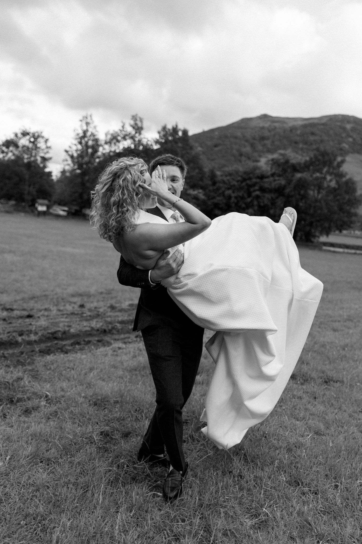 A playful wedding couple dances in a meadow with mountains visible in the distance.