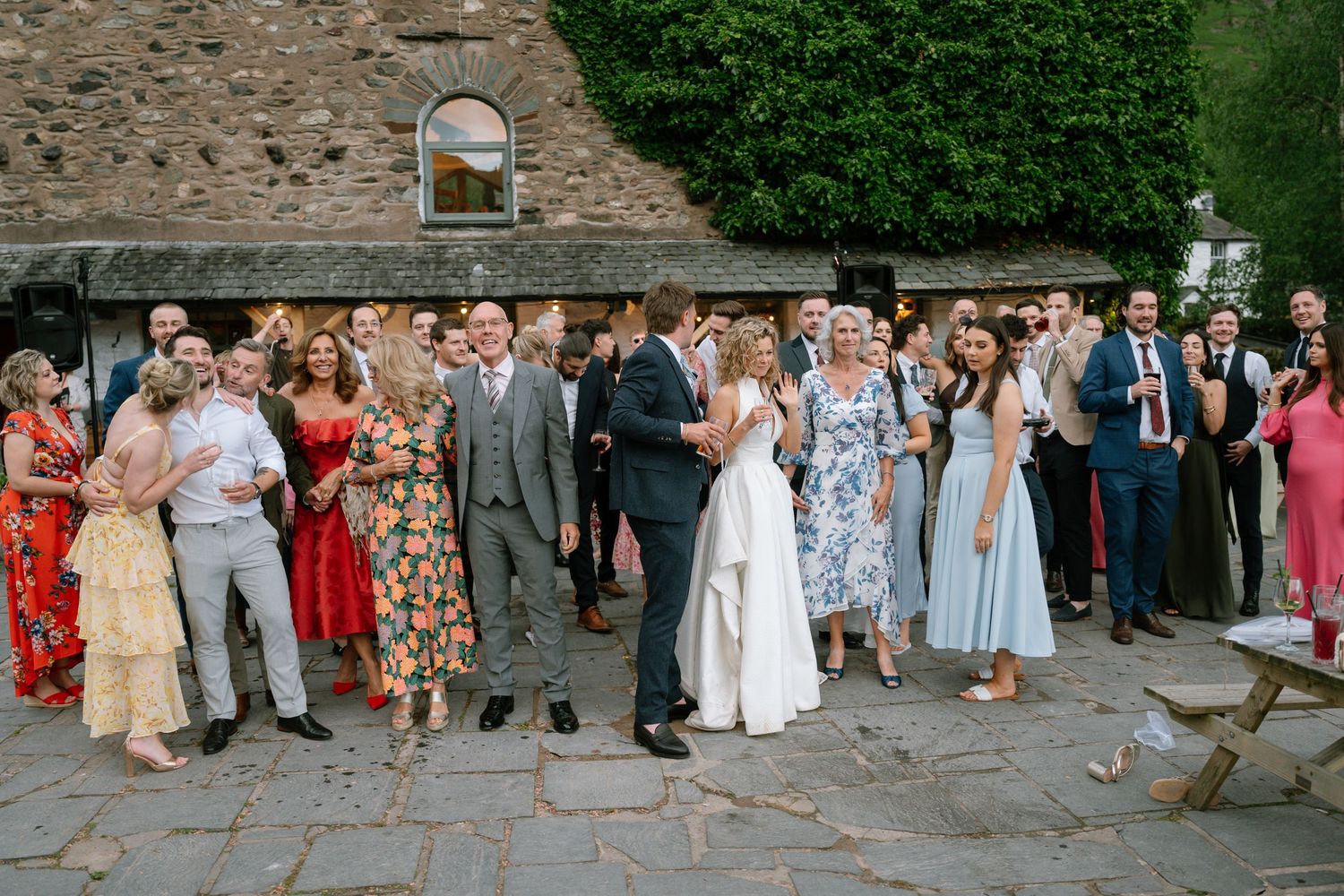 Wedding guests gathered outside a stone building for a group photo during the celebration.