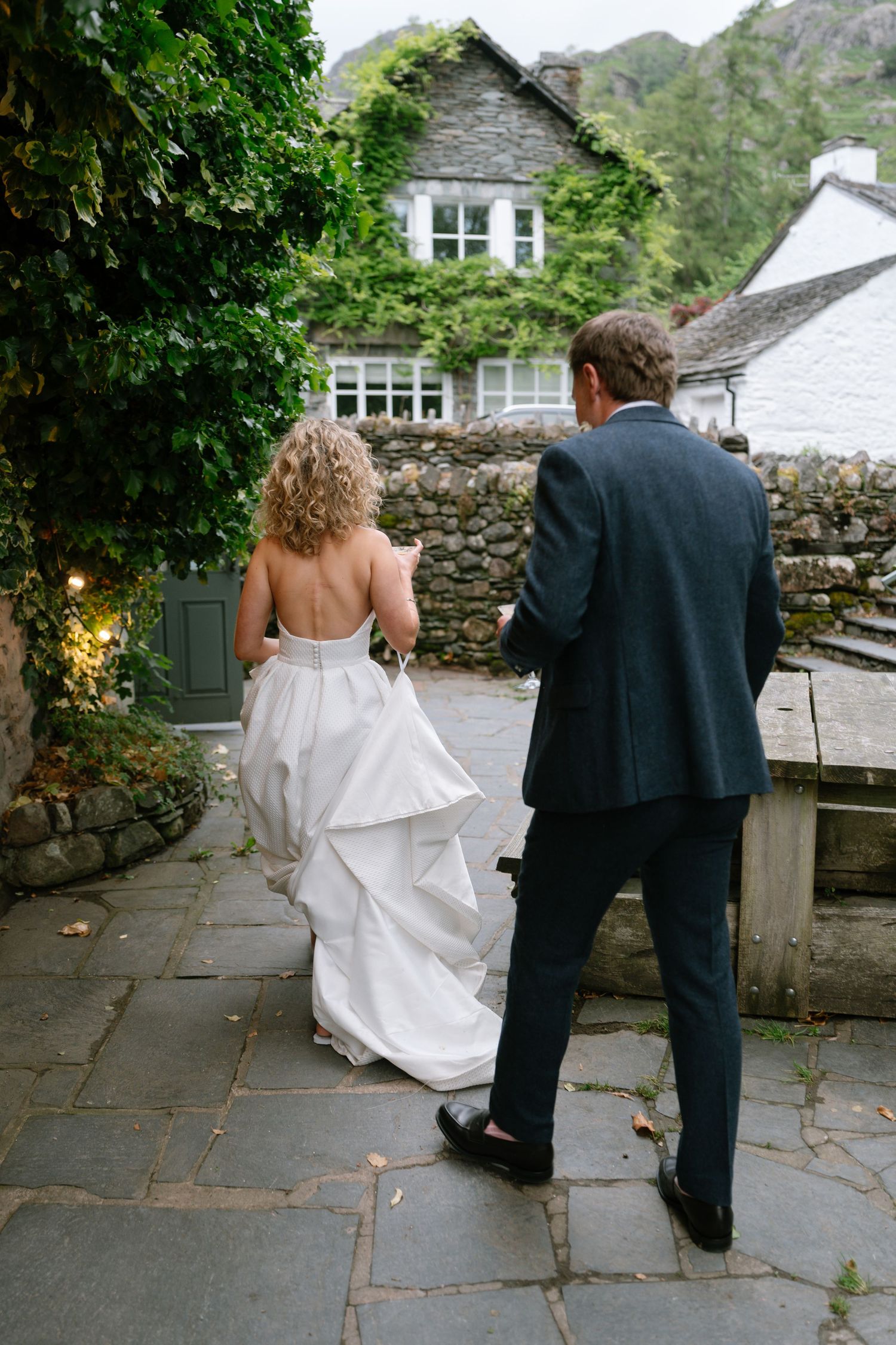 Couple walking along stone pathway surrounded by lush greenery and mountain views.