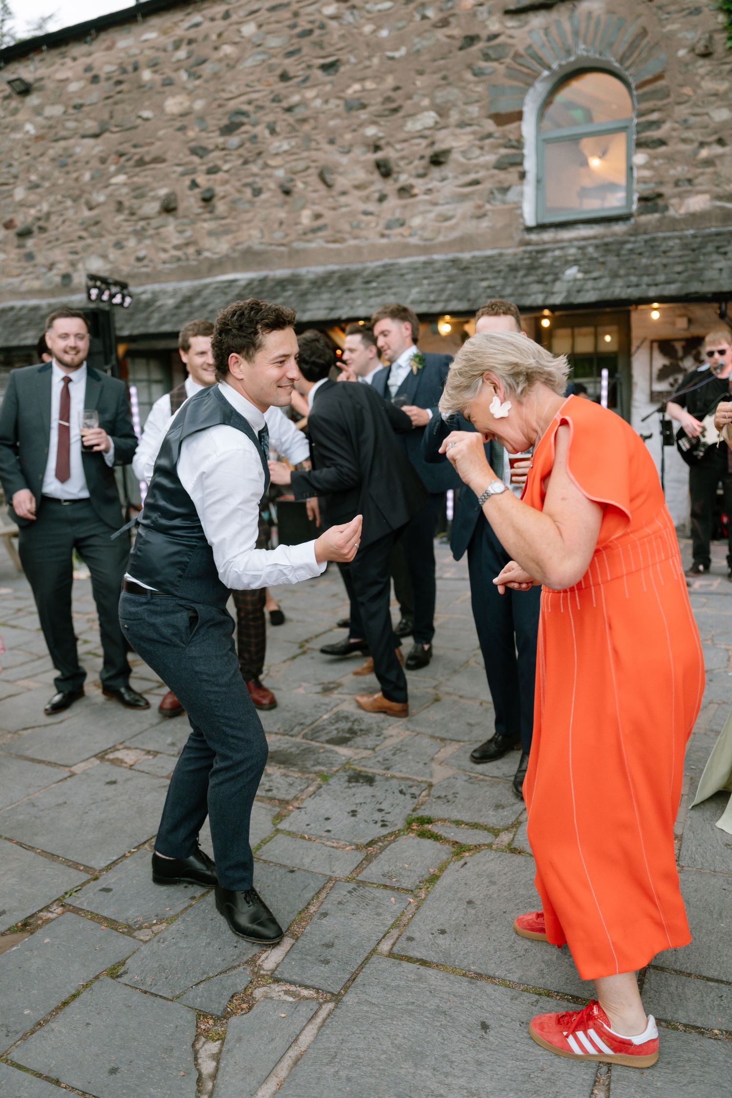 Energetic dancing scene at wedding reception outside stone building.