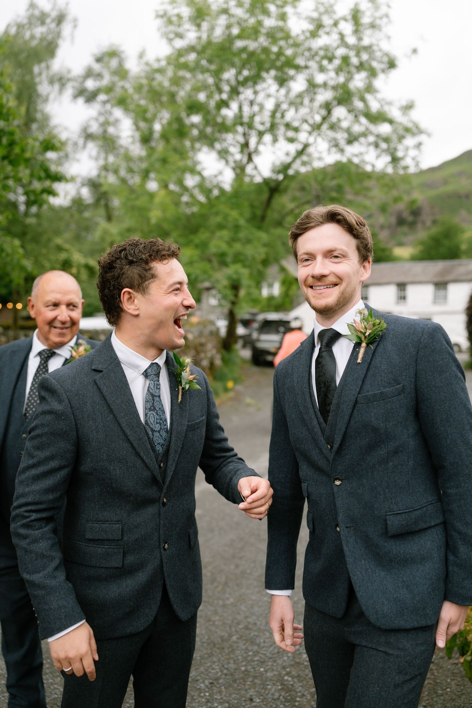 Groomsmen in dark suits share laughs and candid moments outside during a wedding celebration.