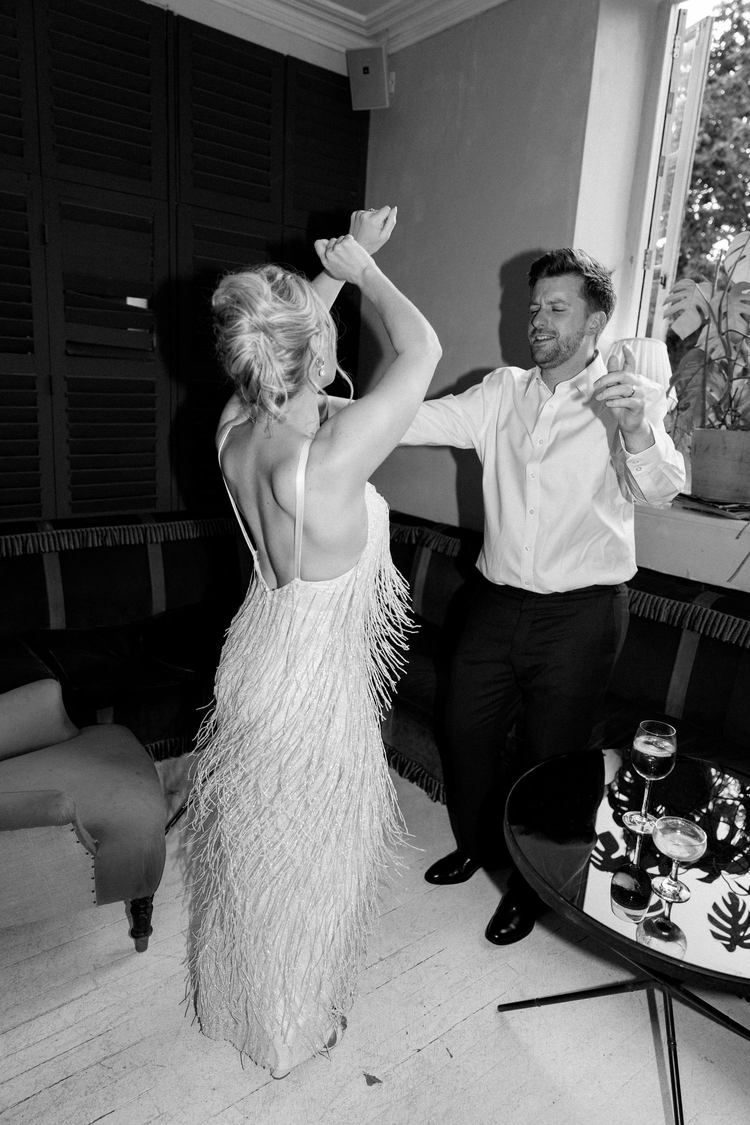 A couple dancing together in a room, with the woman wearing a fringed white dress.