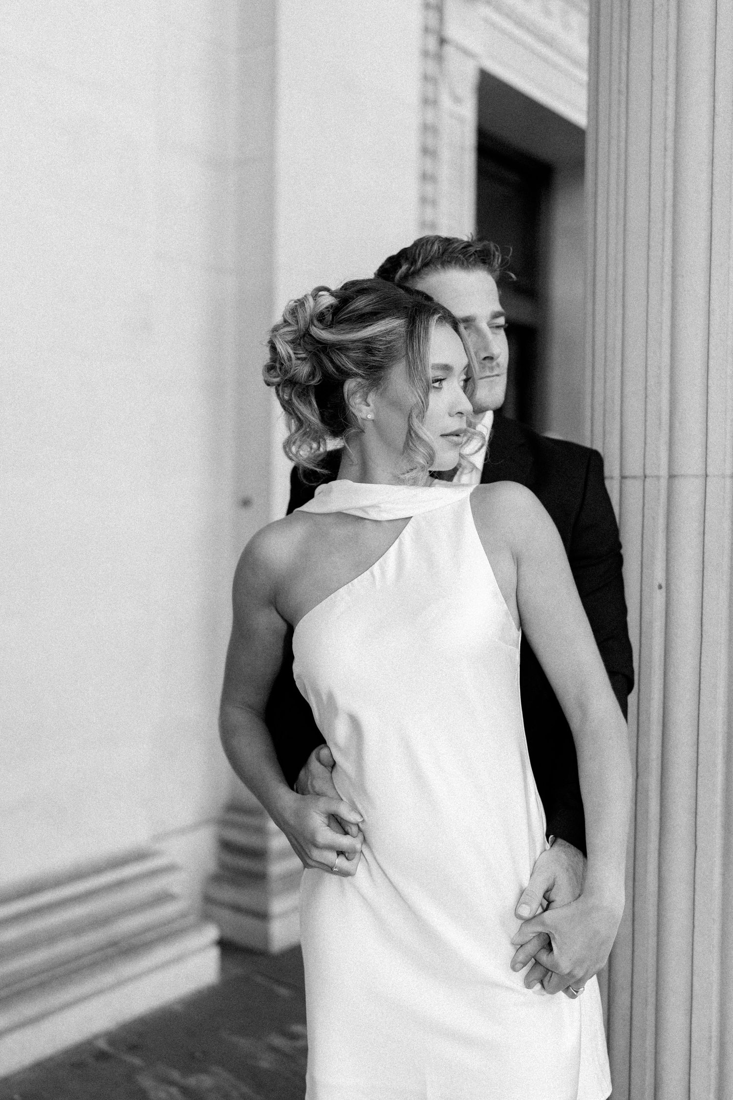 Tender embrace captured in black and white against architectural columns.