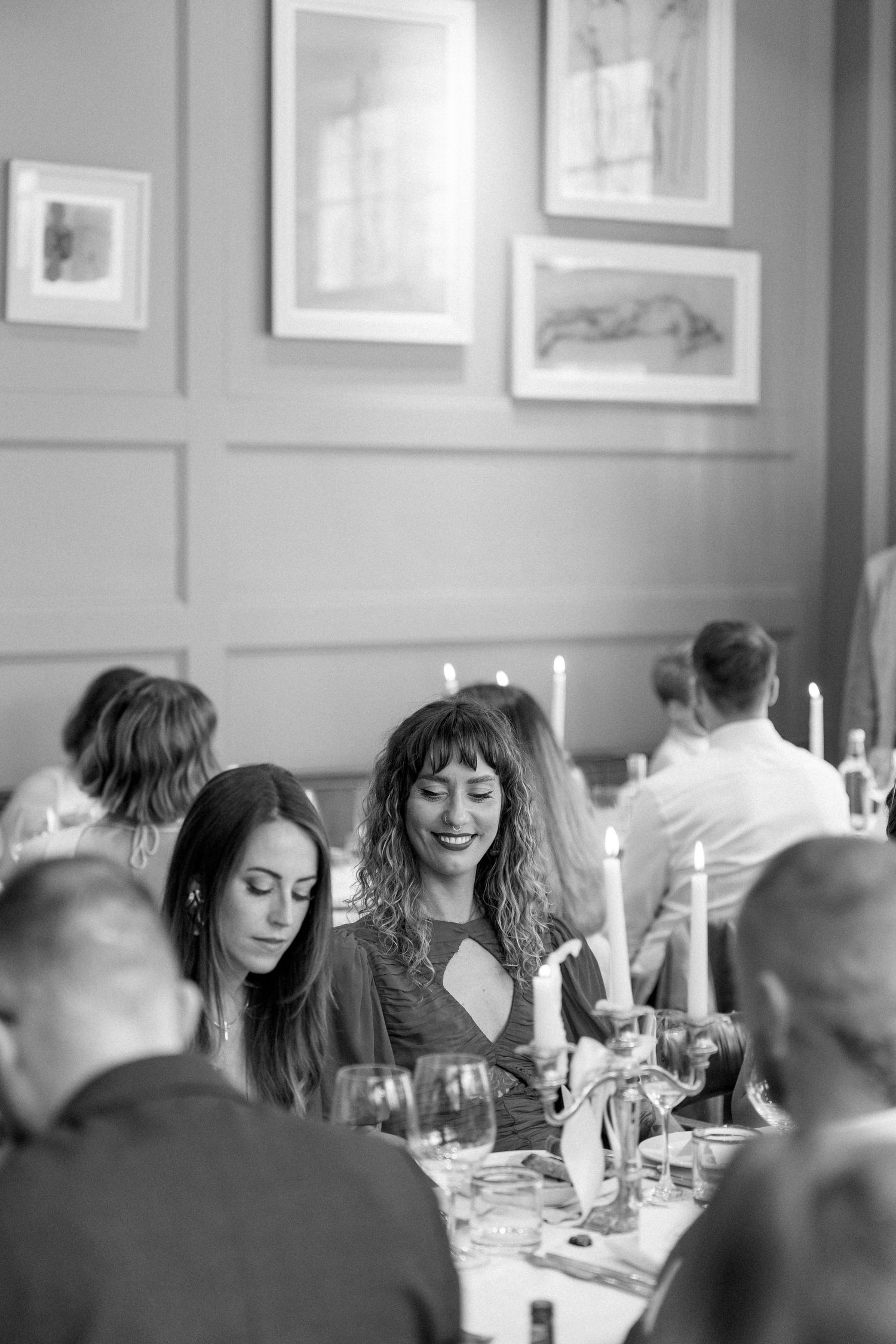 Black and white photo of dinner guests enjoying conversation at candlelit wedding reception.