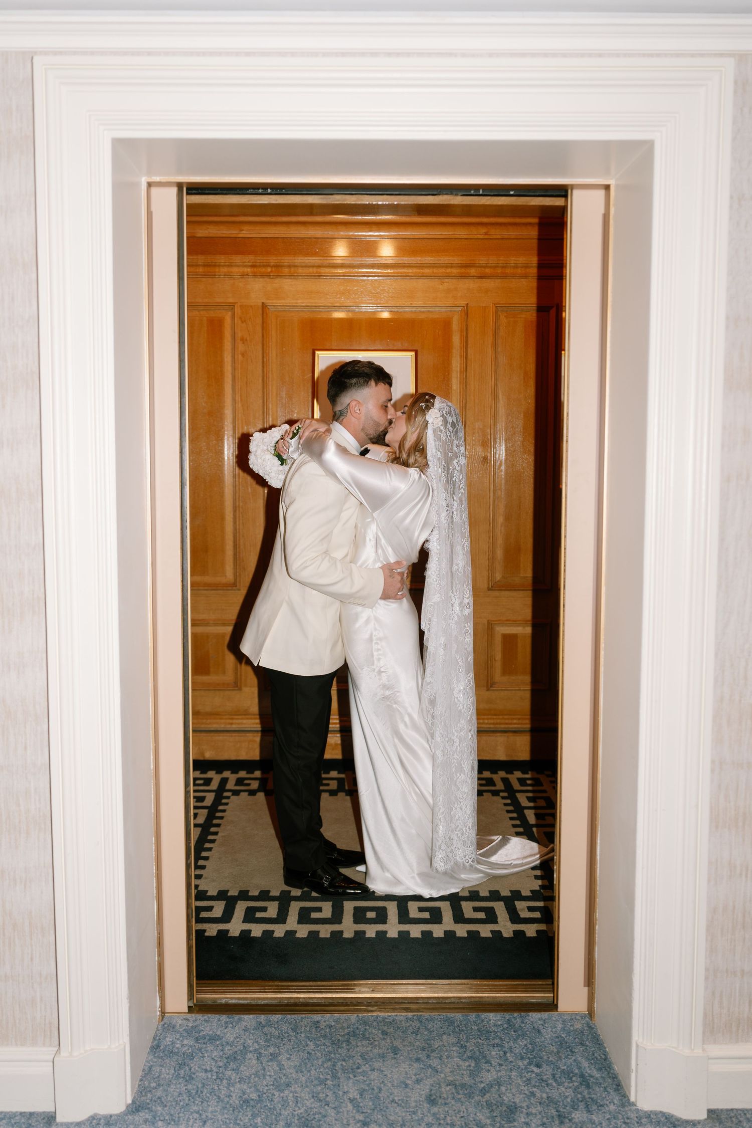 Romantic moment between newlyweds in white attire captured in an ornate doorway.