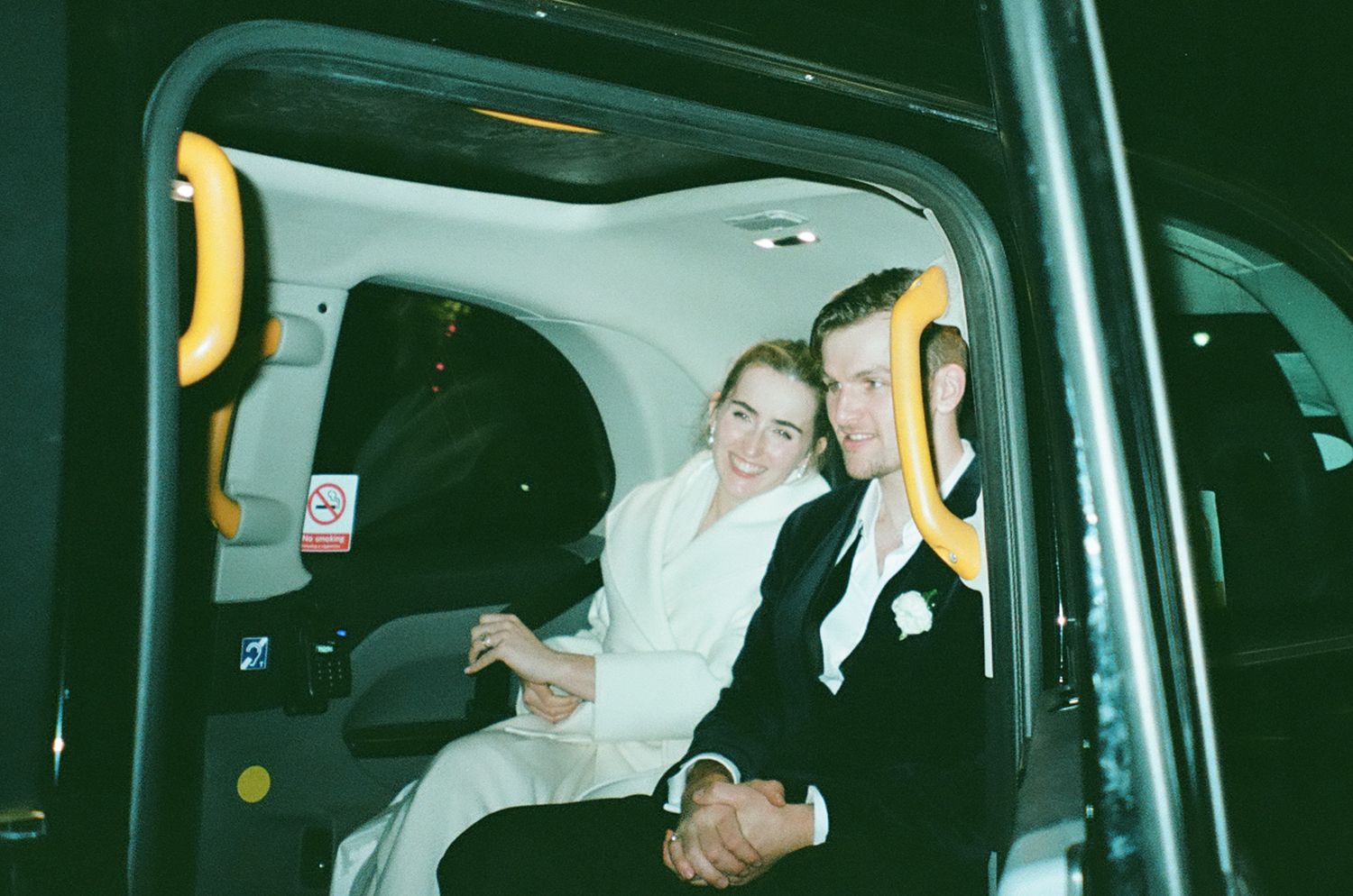Wedding party inside a vehicle with festive expressions and formal attire.