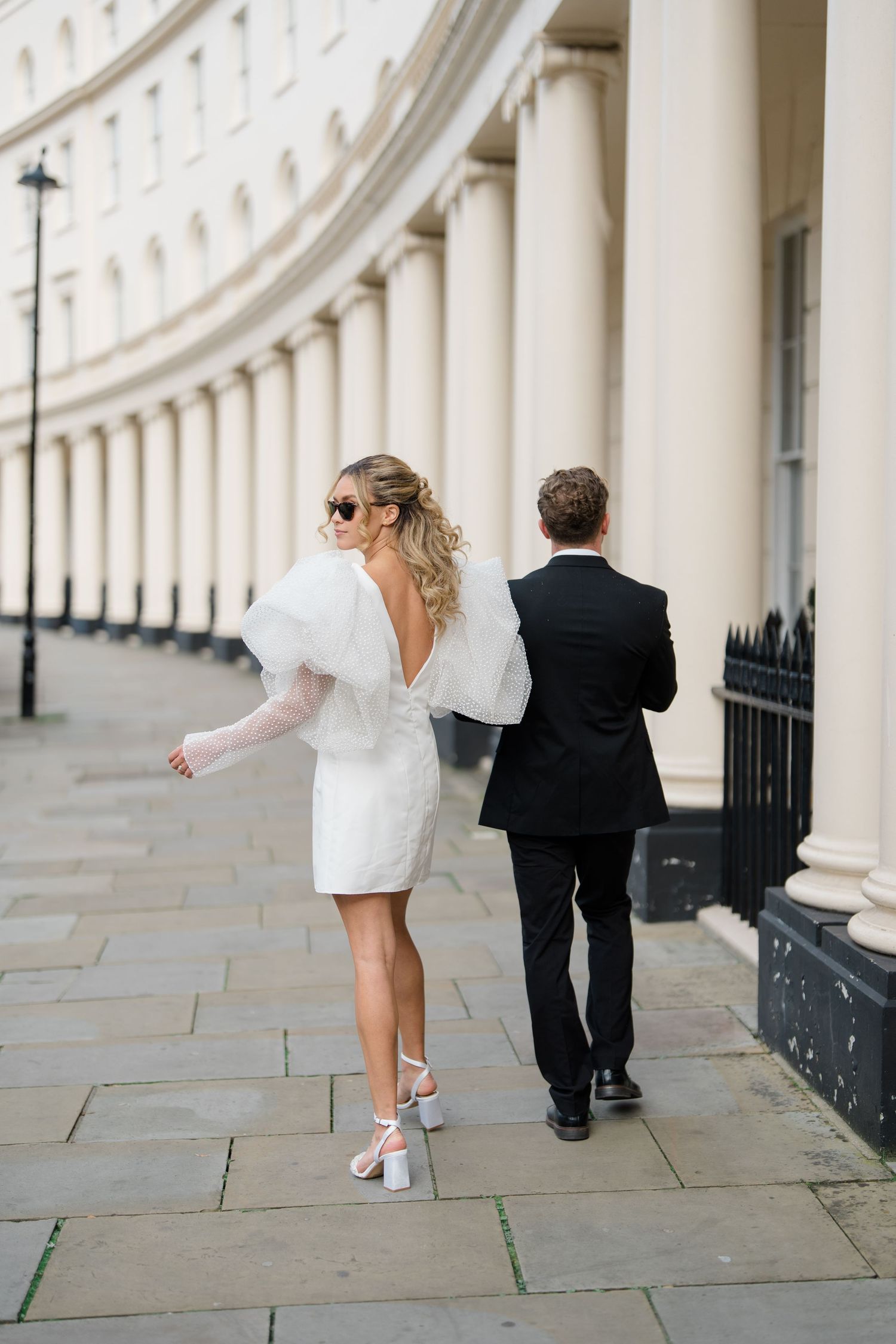 A couple walking and dancing along a curved colonnade with classic architecture.