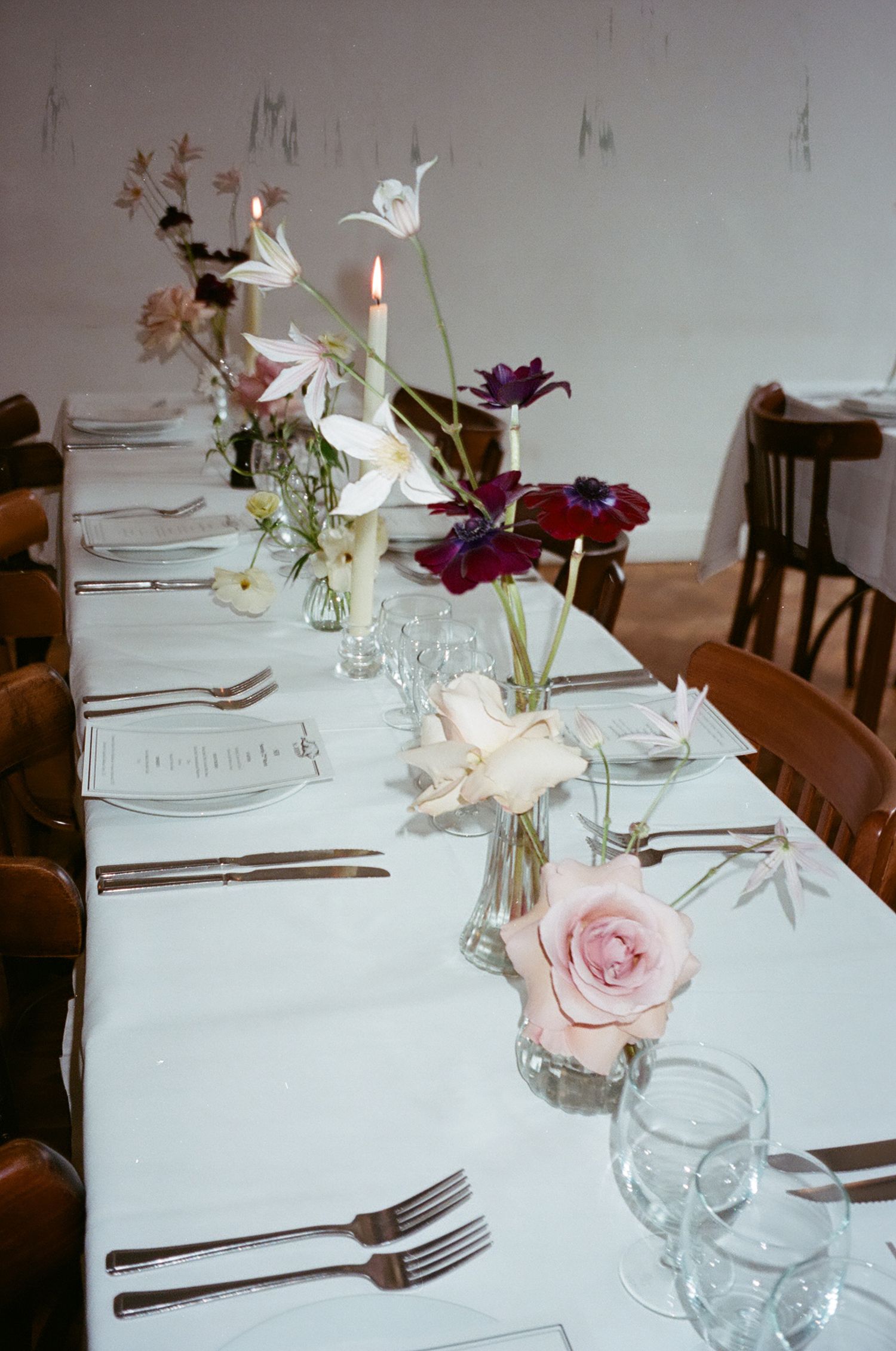 Elegant table settings with white linens, wine glasses, and delicate floral centerpieces featuring pink roses and lilies.