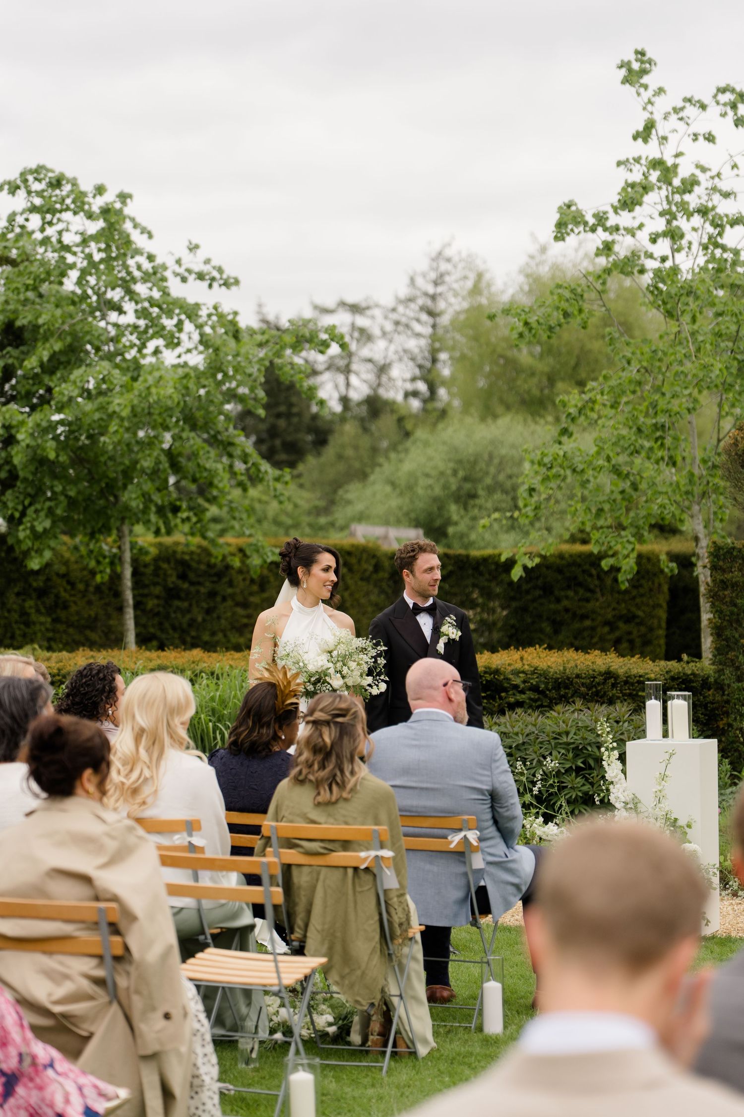 Bride and groom standing at outdoor wedding ceremony surrounded by lush garden hedges.