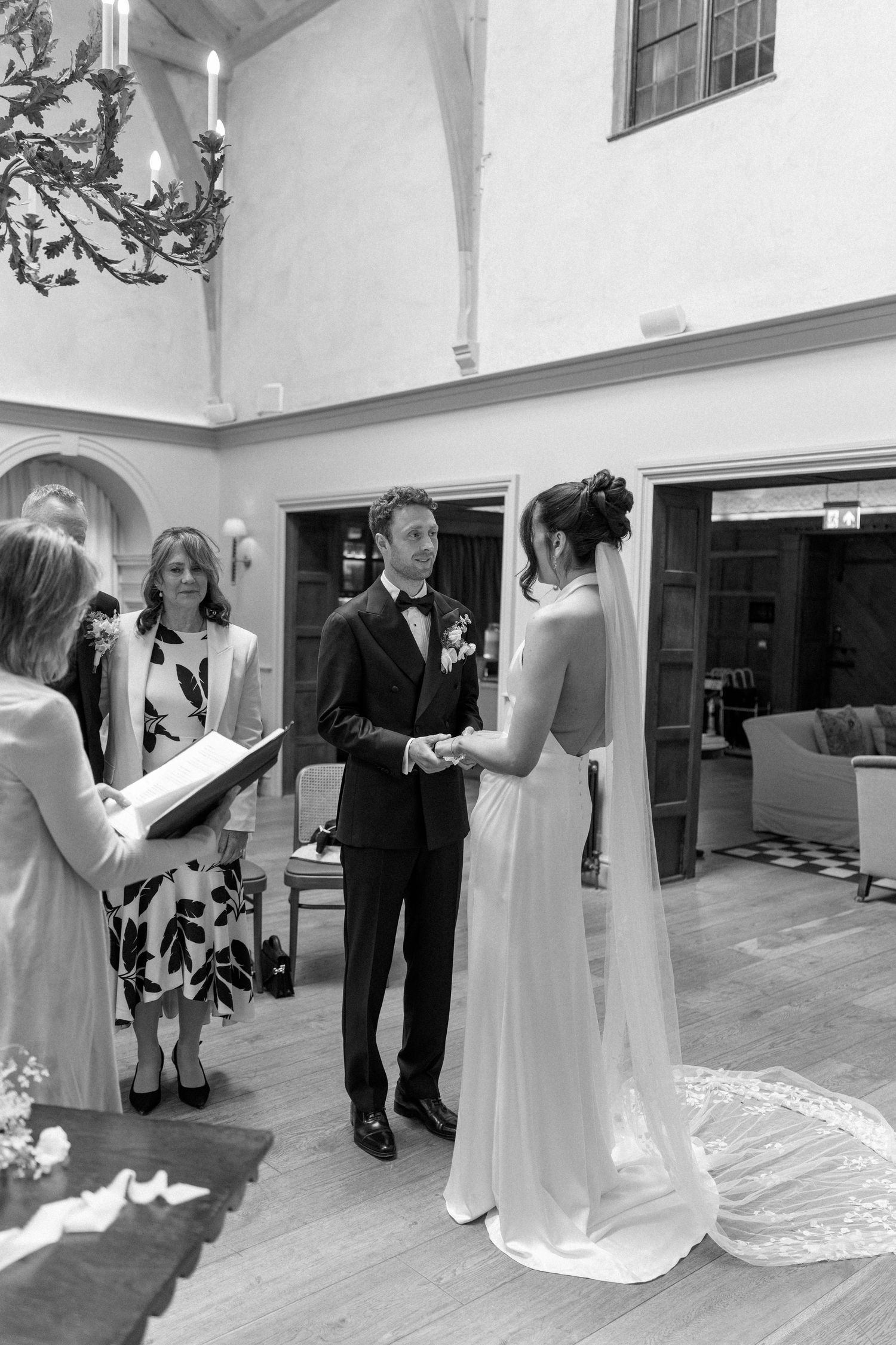 Bride and groom exchanging vows at indoor wedding ceremony in black and white photography.