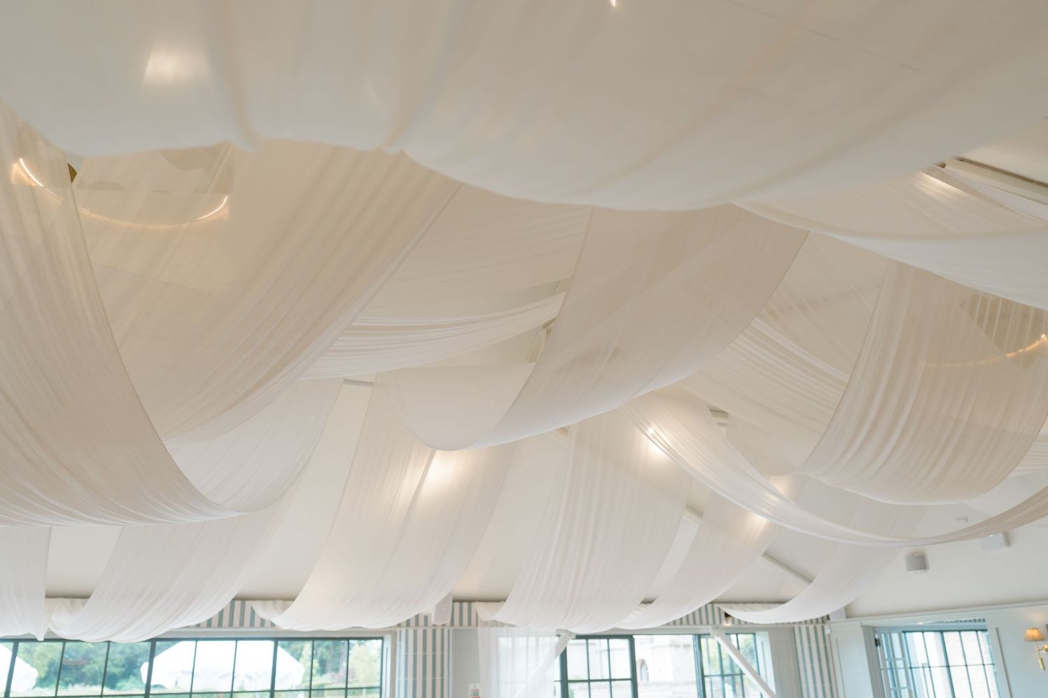 Stunning white fabric ceiling draping with soft lighting in elegant wedding reception venue.