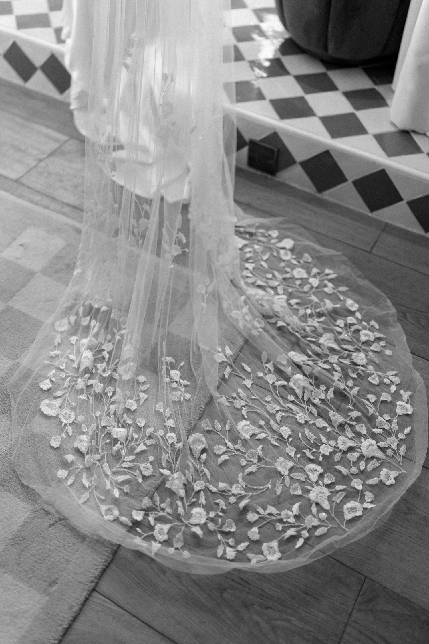 Black and white detail of floral embroidered wedding veil spread on wooden floor.
