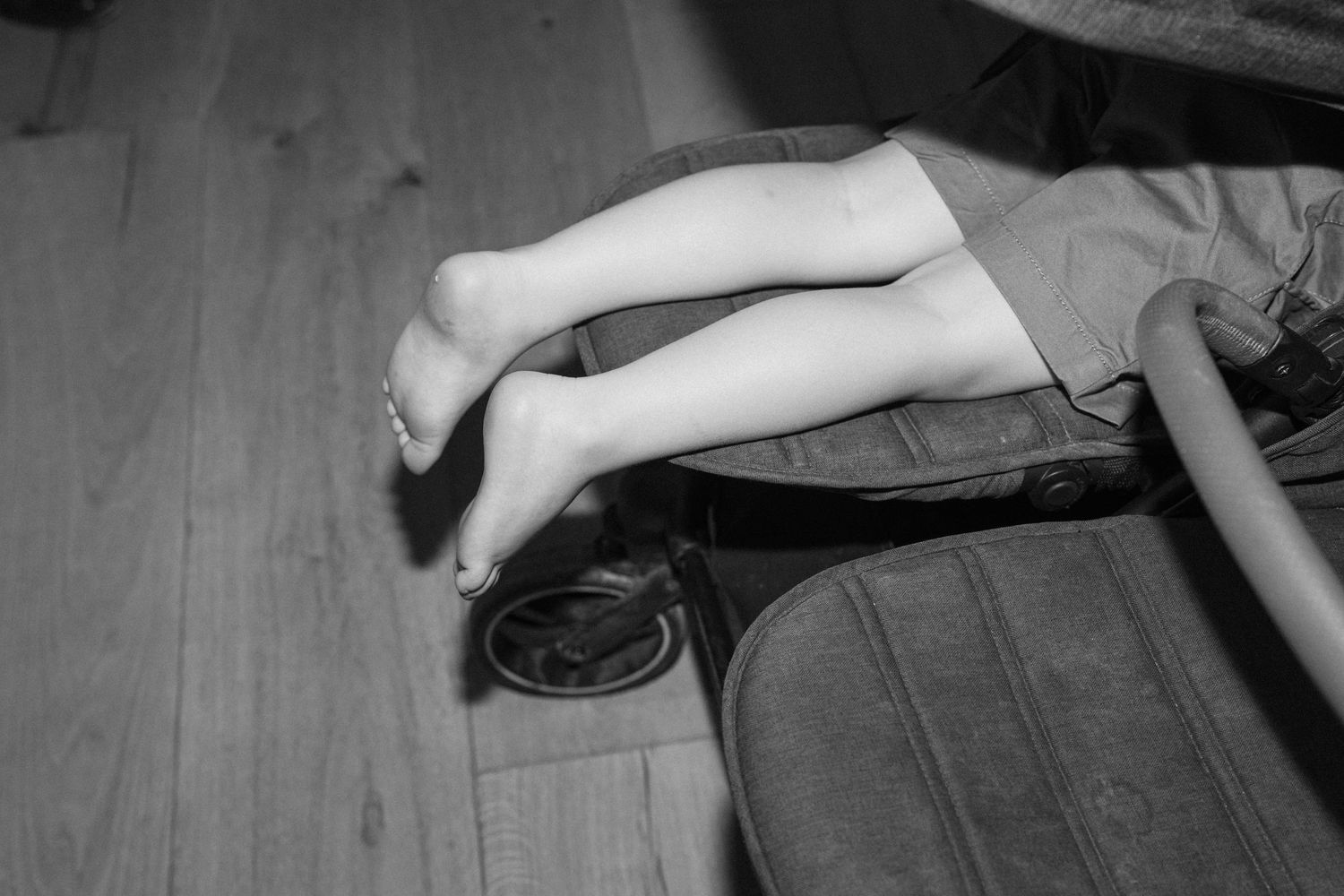 Black and white close-up of brides bare feet resting on luggage on wooden floor after wedding celebration.