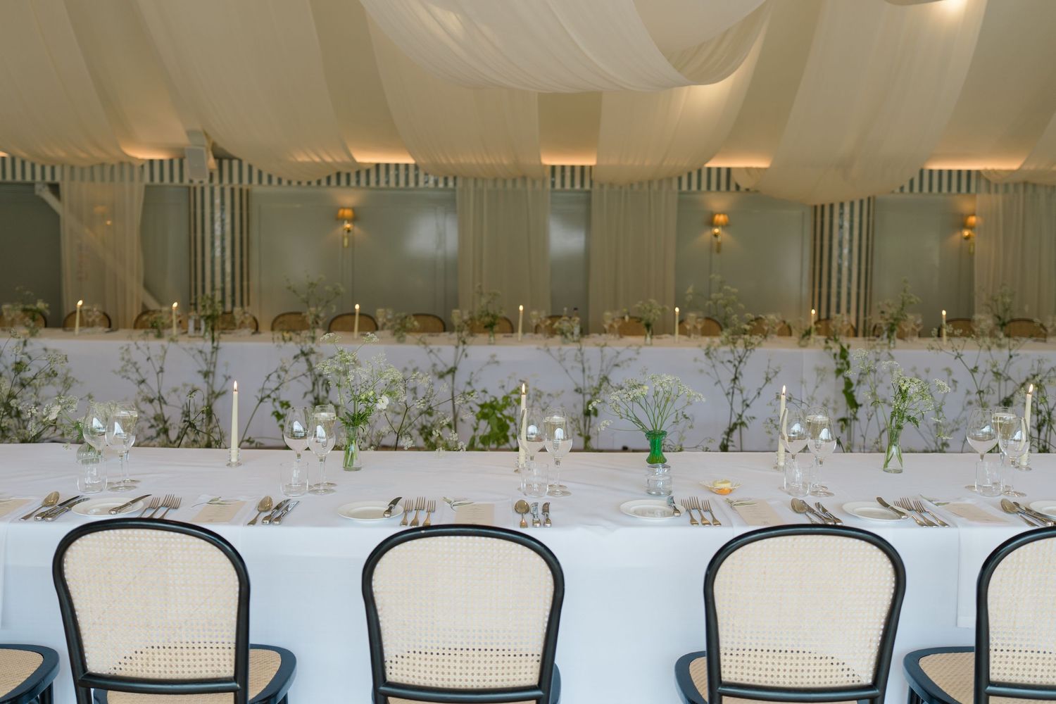 Elegant wedding reception table setup with white linens, candles and greenery centerpieces.
