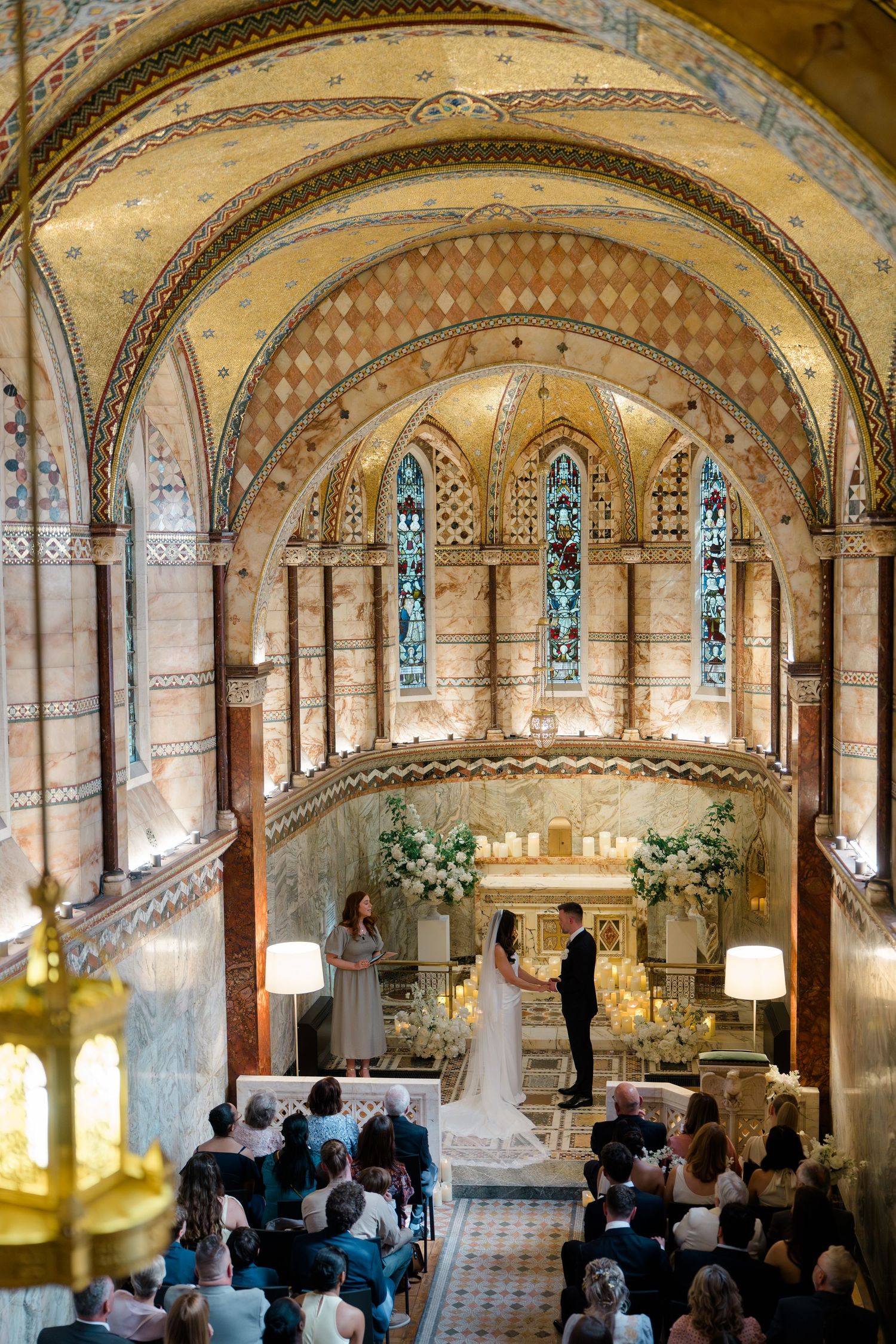 Aerial view of bride and groom exchanging vows in stunning ornate chapel with arched ceilings.
