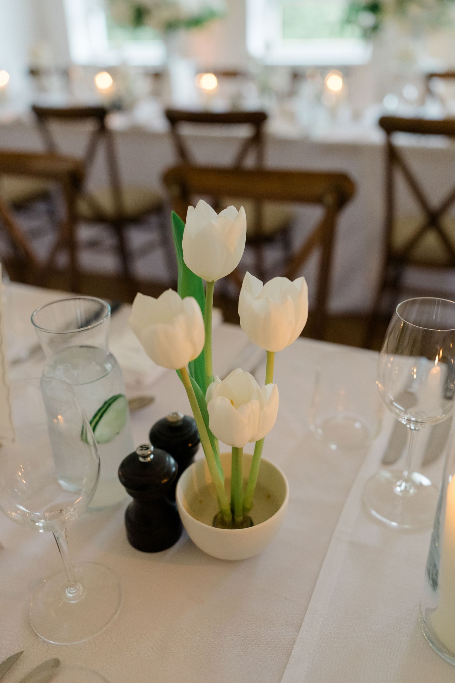 Elegant wedding table centerpiece featuring white tulips in a small pot beside salt and pepper shakers and glassware.