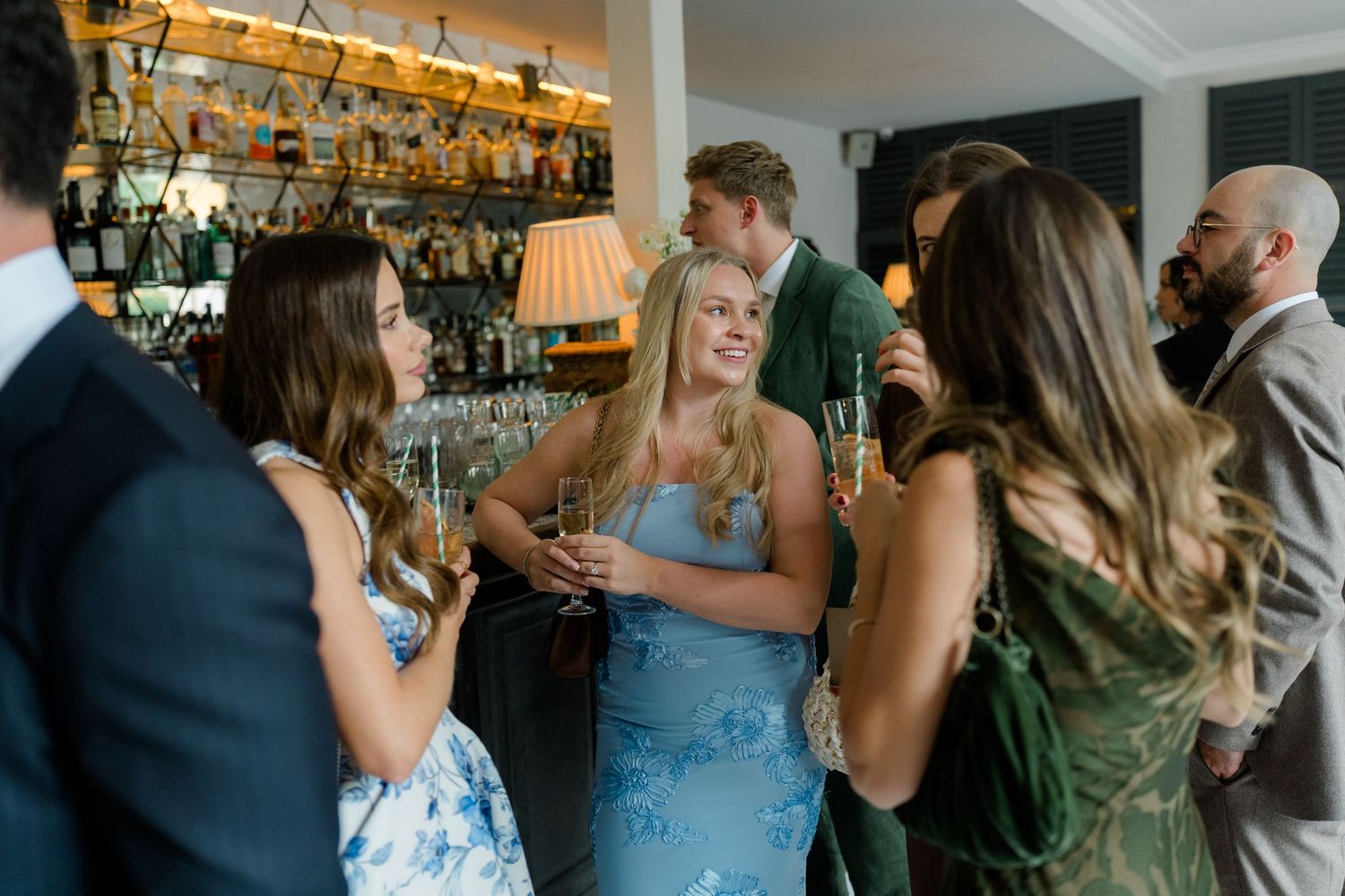 Wedding guests in elegant attire socializing and drinking champagne at a stylish bar reception.