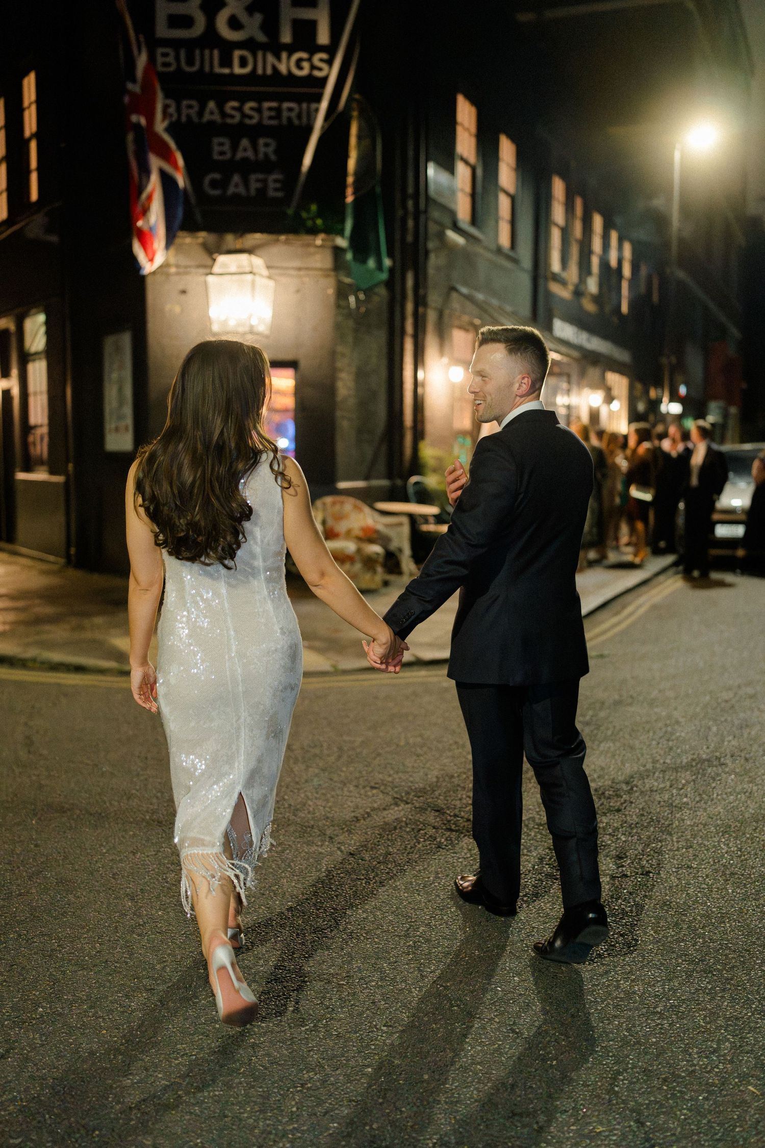 Bride and groom walking hand in hand at night outside B&H Buildings Brasserie Bar Cafe in London.