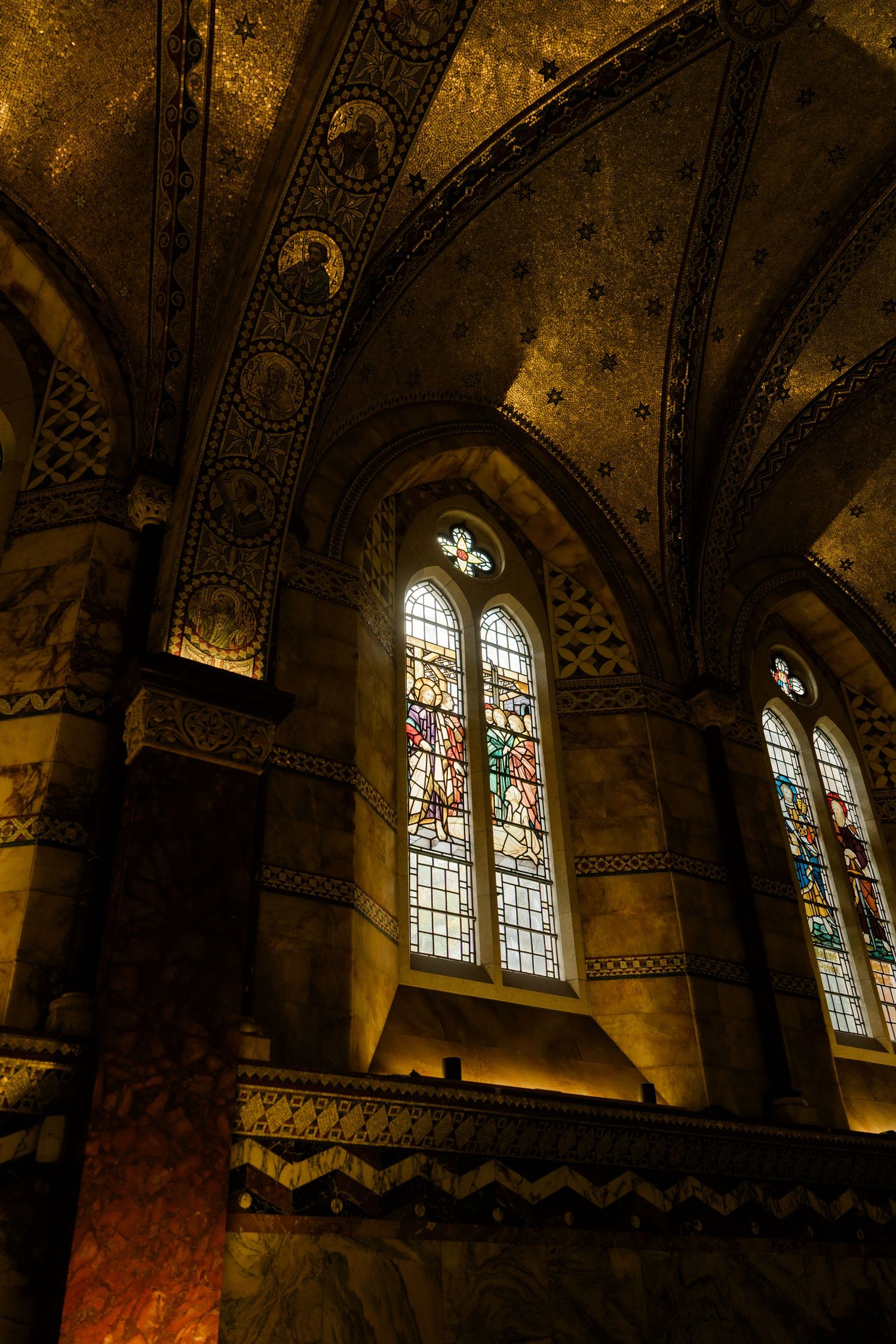 Gothic cathedral interior with ornate arched ceiling, golden mosaics, and colorful stained glass windows.