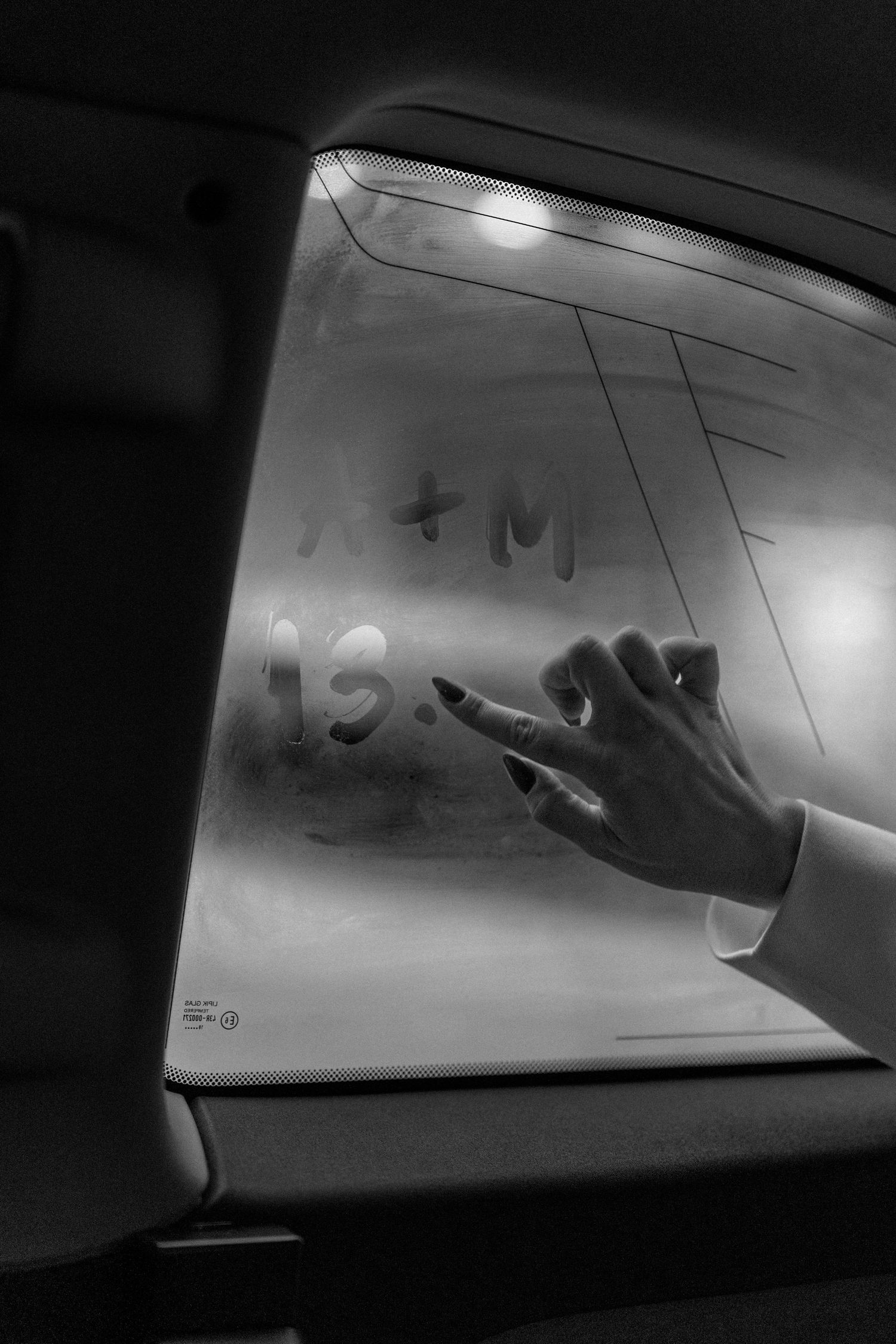 Hand writing initials and date on foggy car window in black and white wedding photo.