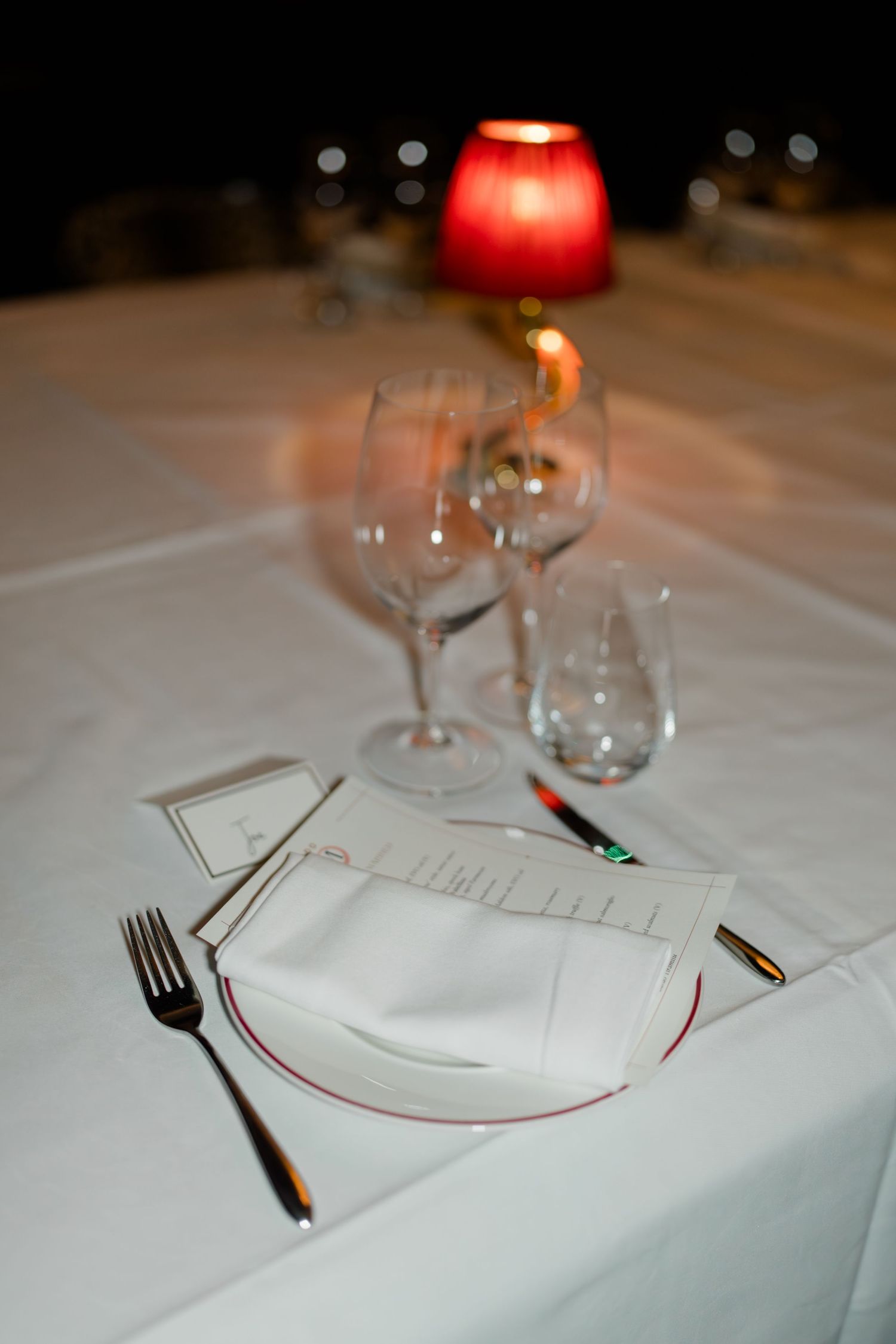 Elegant wedding dinner table setting with red candle, wine glasses, and white linen napkin.