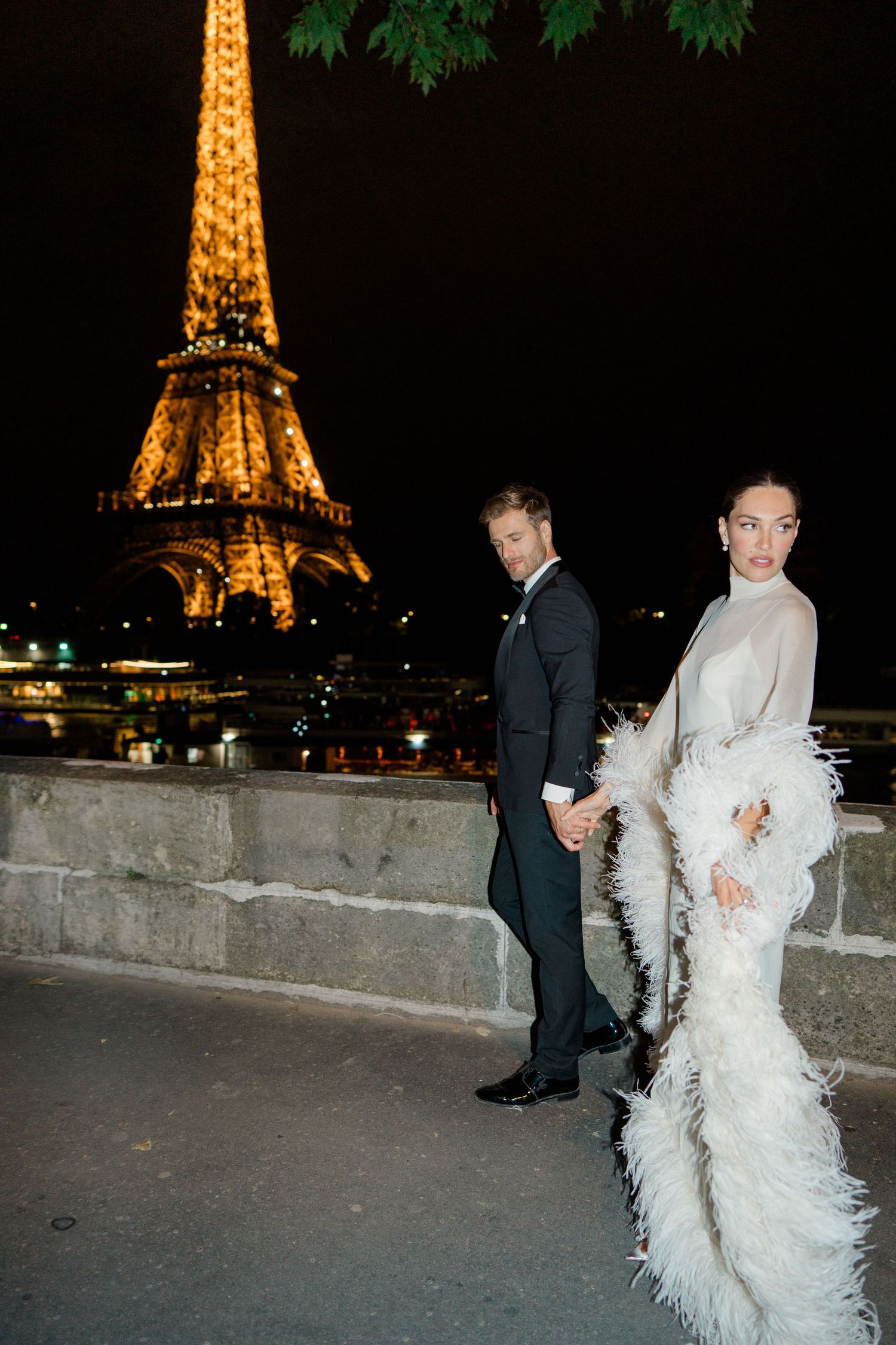 Elegant couple in formal attire posing near the illuminated Eiffel Tower at night in Paris.