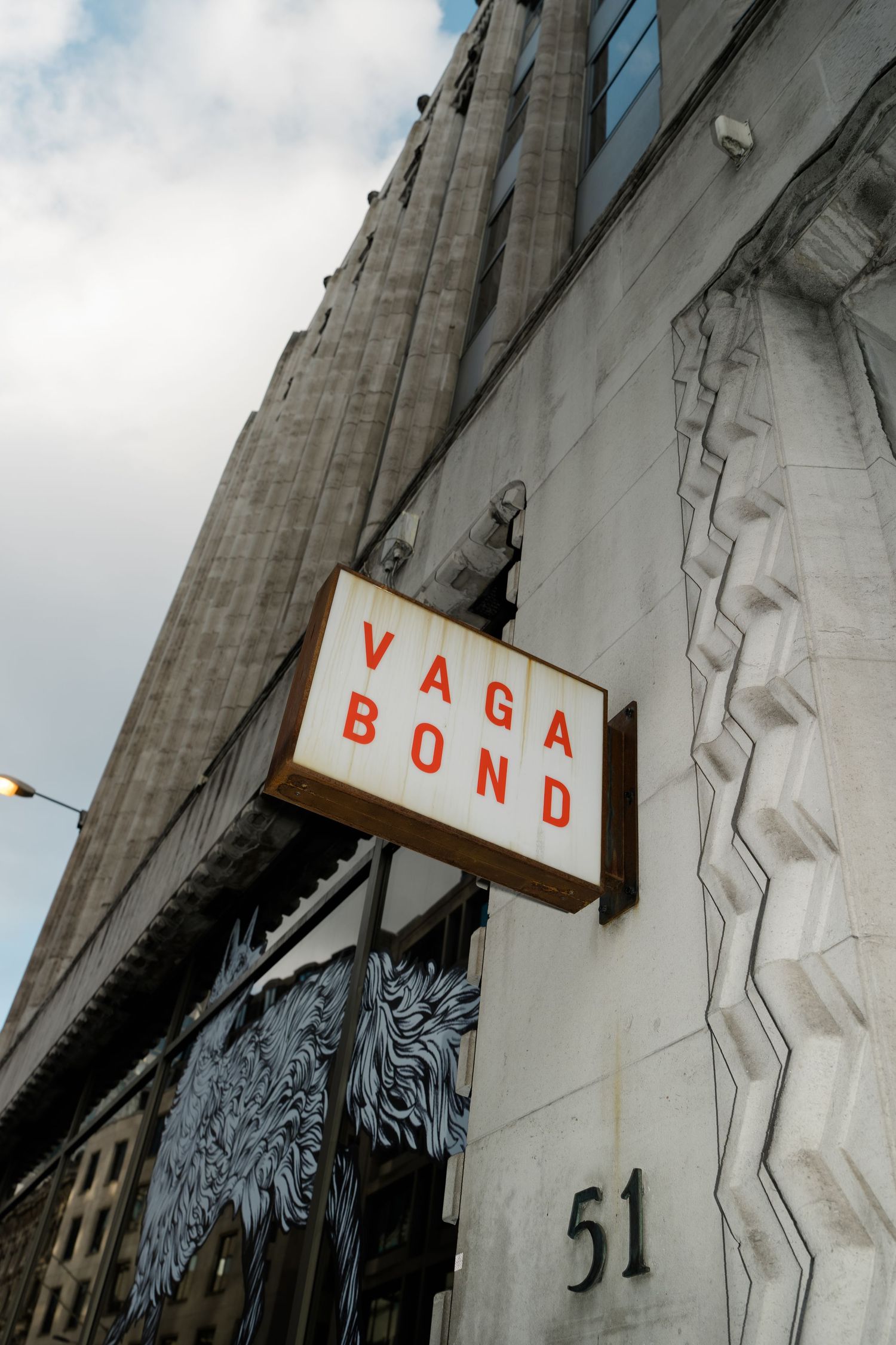 Exterior sign reading Vagabond at number 51 on an Art Deco style building facade.